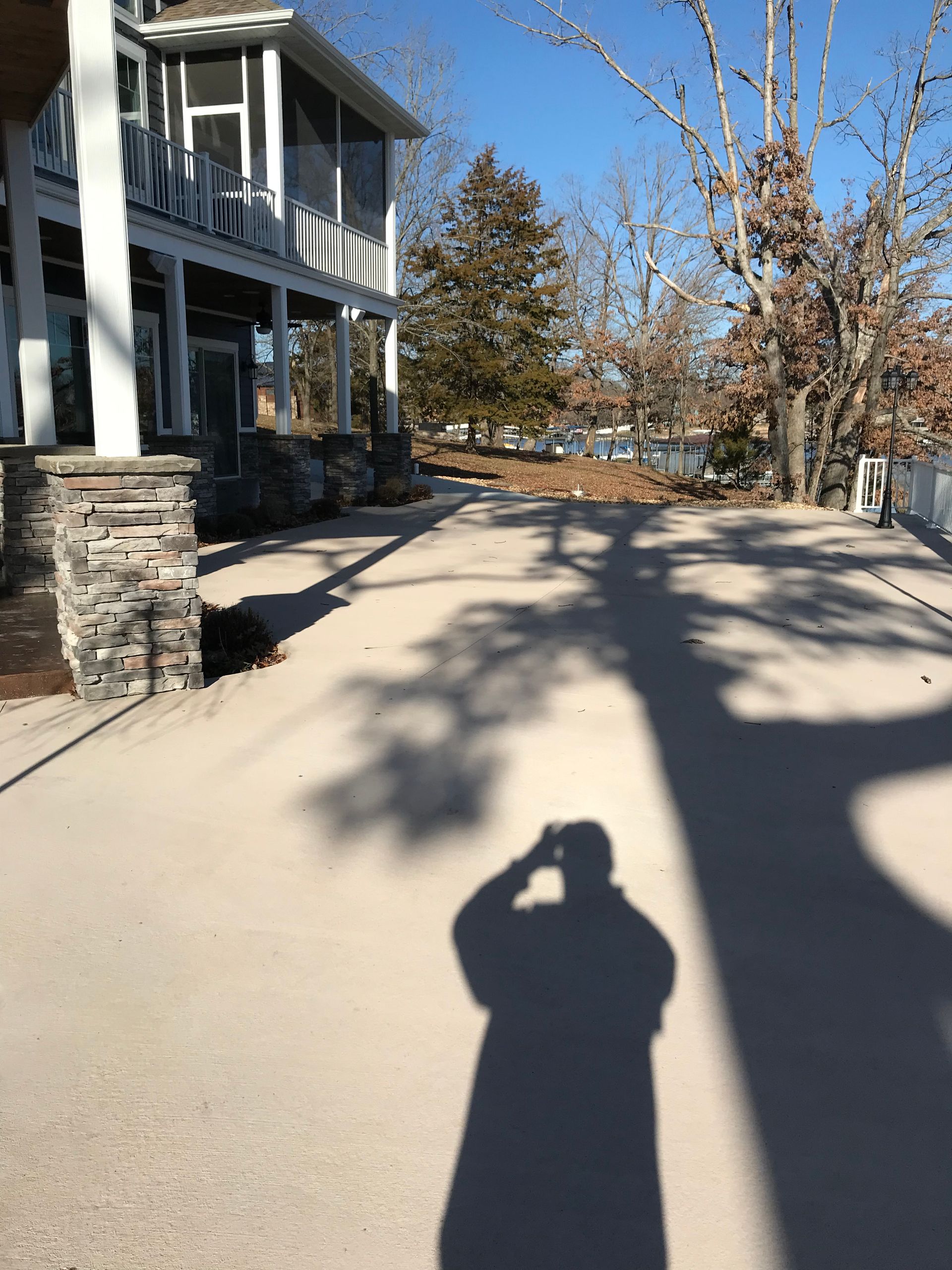 Sunny driveway beside a house, with bare trees and long shadows cast across the pavement.