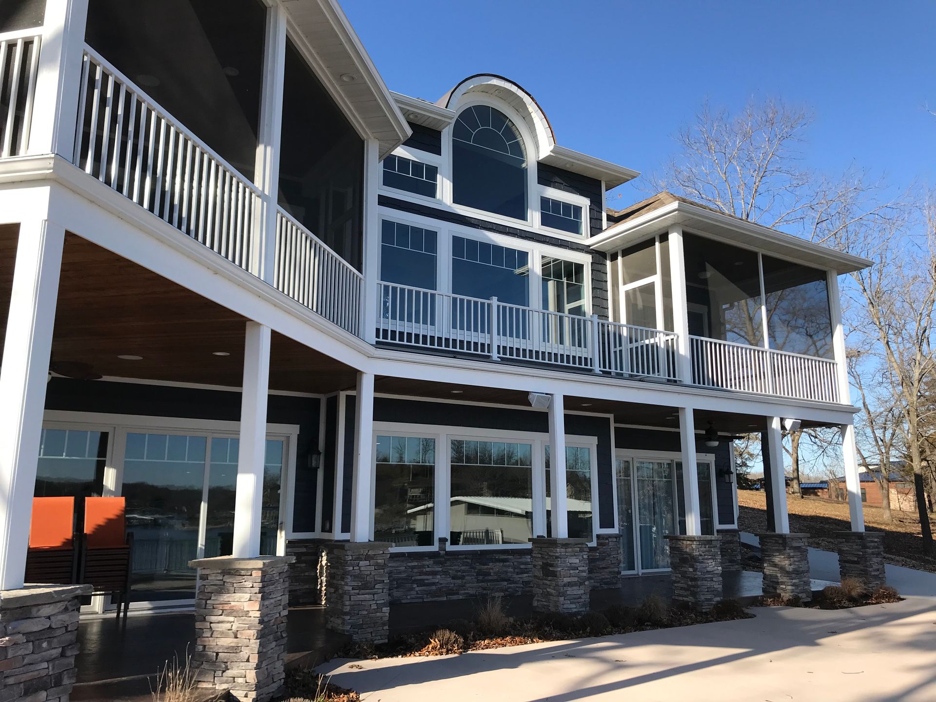 Large two-story house with white balconies, stone columns, and blue sky reflected in tall windows