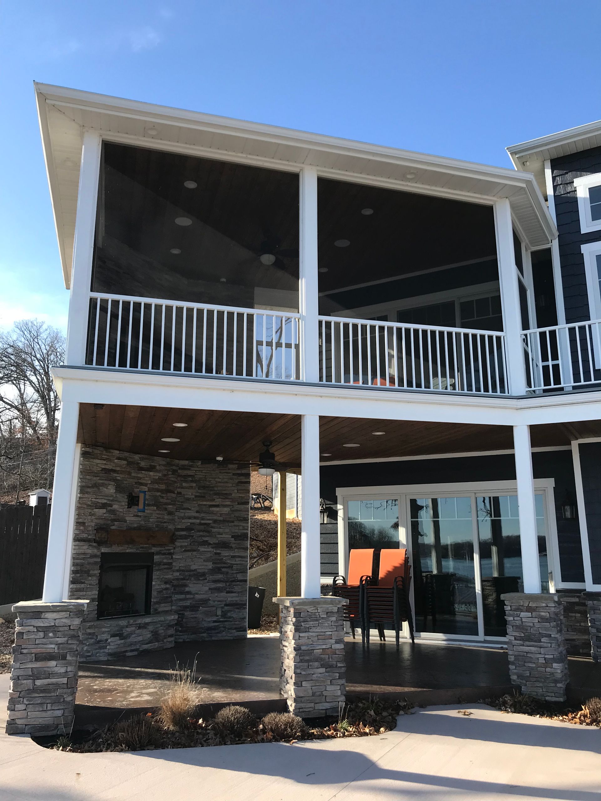 Two-story white house with stone columns and a covered balcony on a sunny day