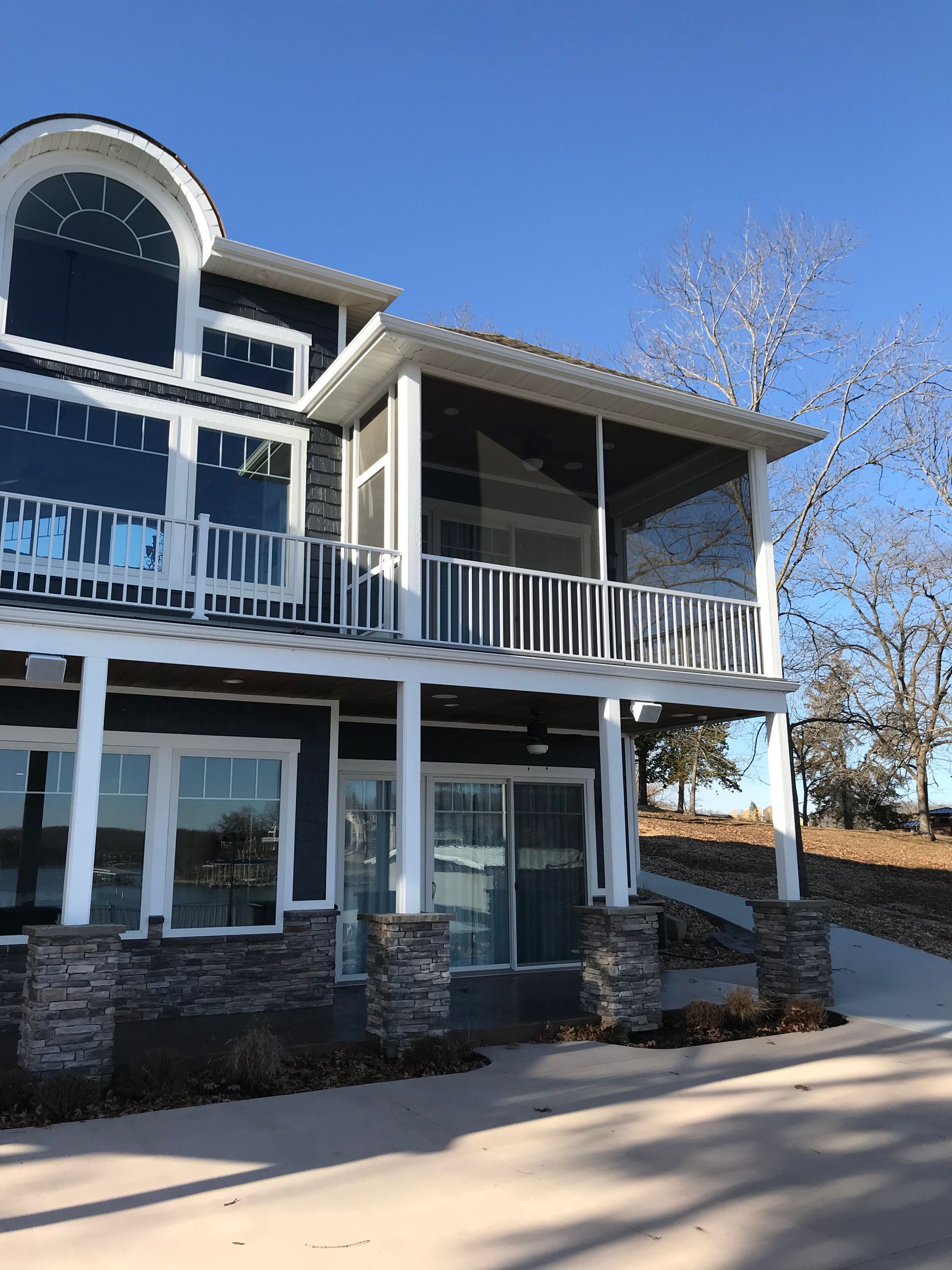 Three-story white house with large balconies and stone foundation under a clear blue sky