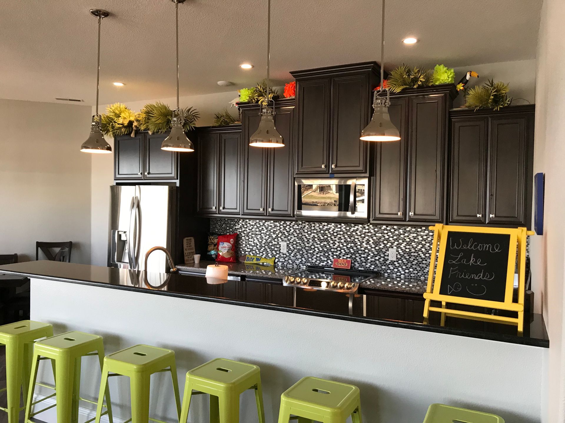 Modern kitchen with black cabinets, mosaic backsplash, white island, and green stools.