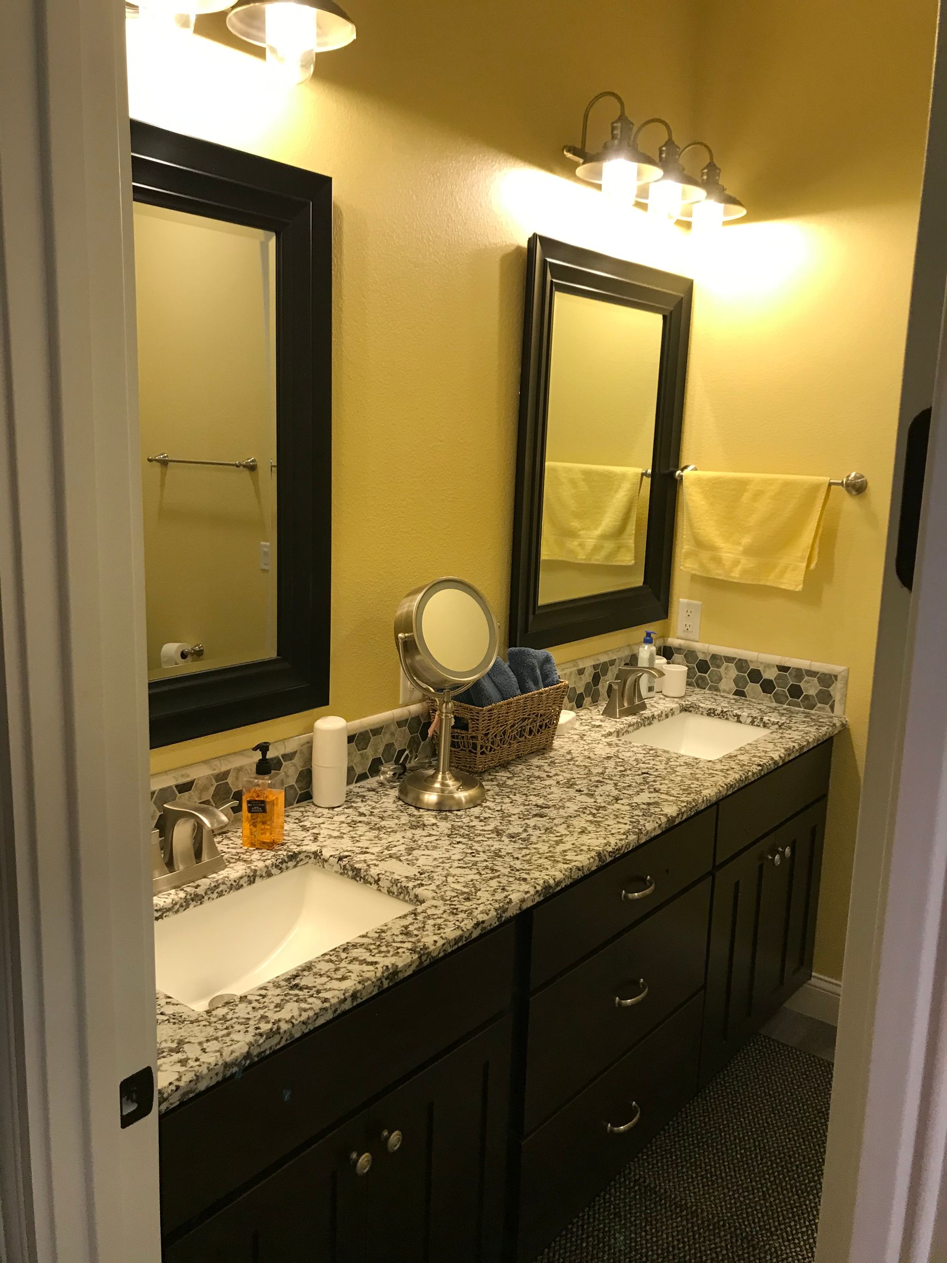 Bathroom vanity with double sinks, granite countertop, mirrors, and warm wall lighting