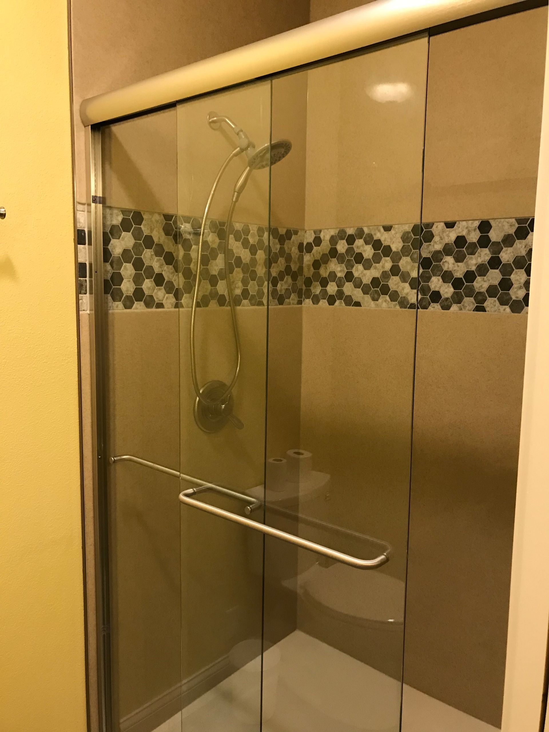 Glass shower stall with beige tile and a mosaic accent strip, plus chrome grab bars and showerhead.