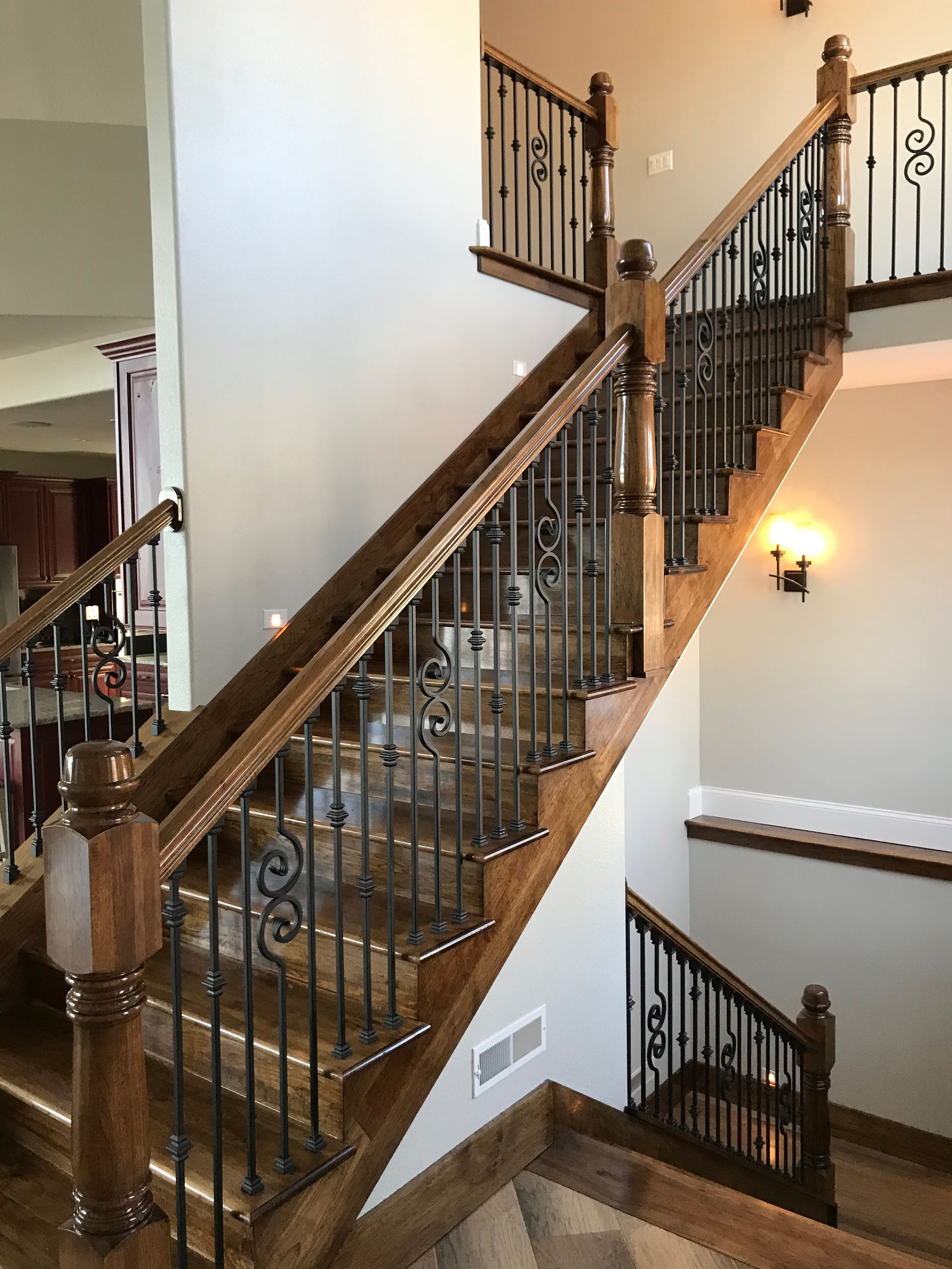 Grand staircase with dark wood banister, metal balusters, and wall sconces in a home interior
