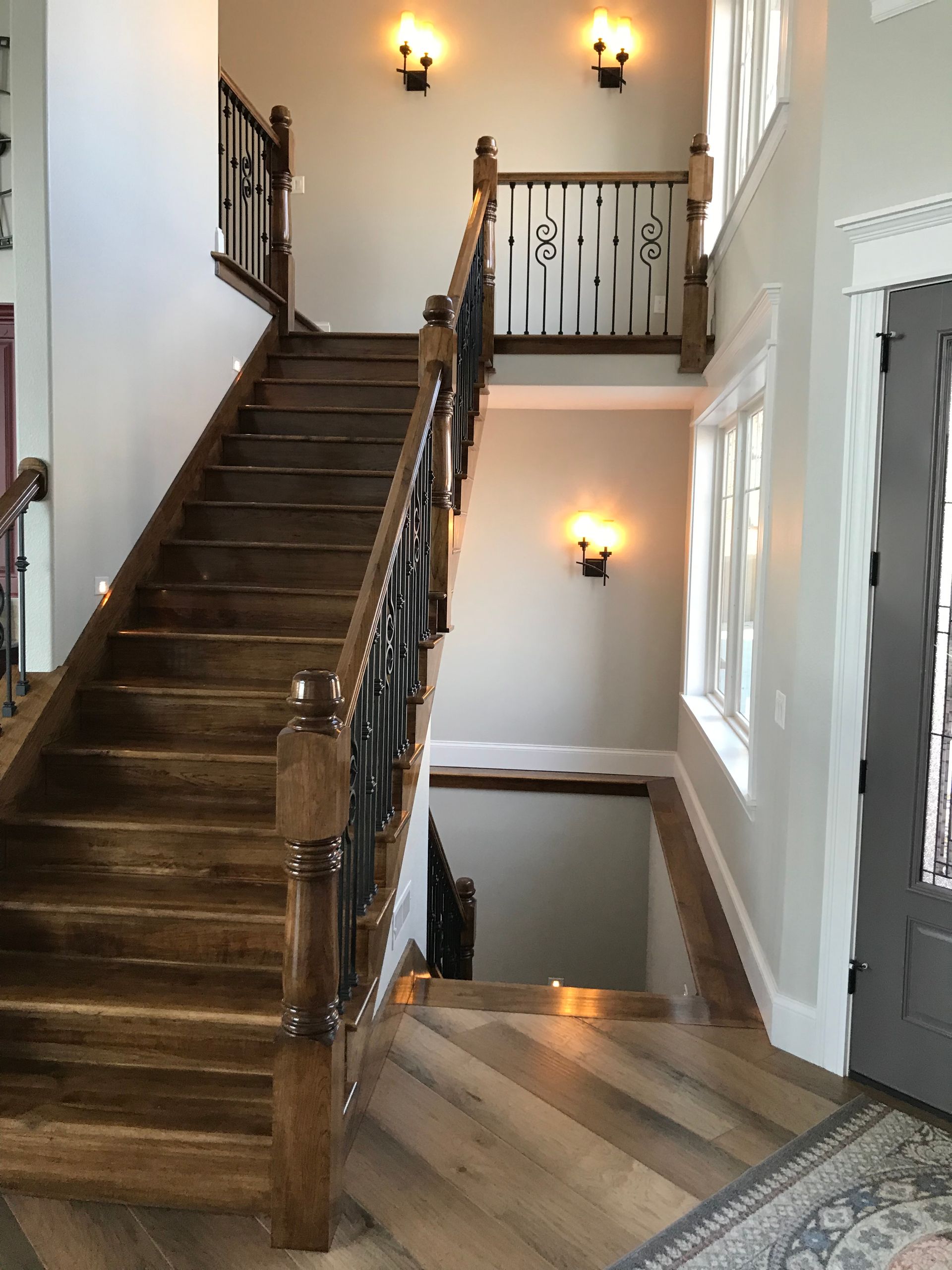Interior stairwell with dark wood stairs, white walls, wrought-iron railing, and wall sconces
