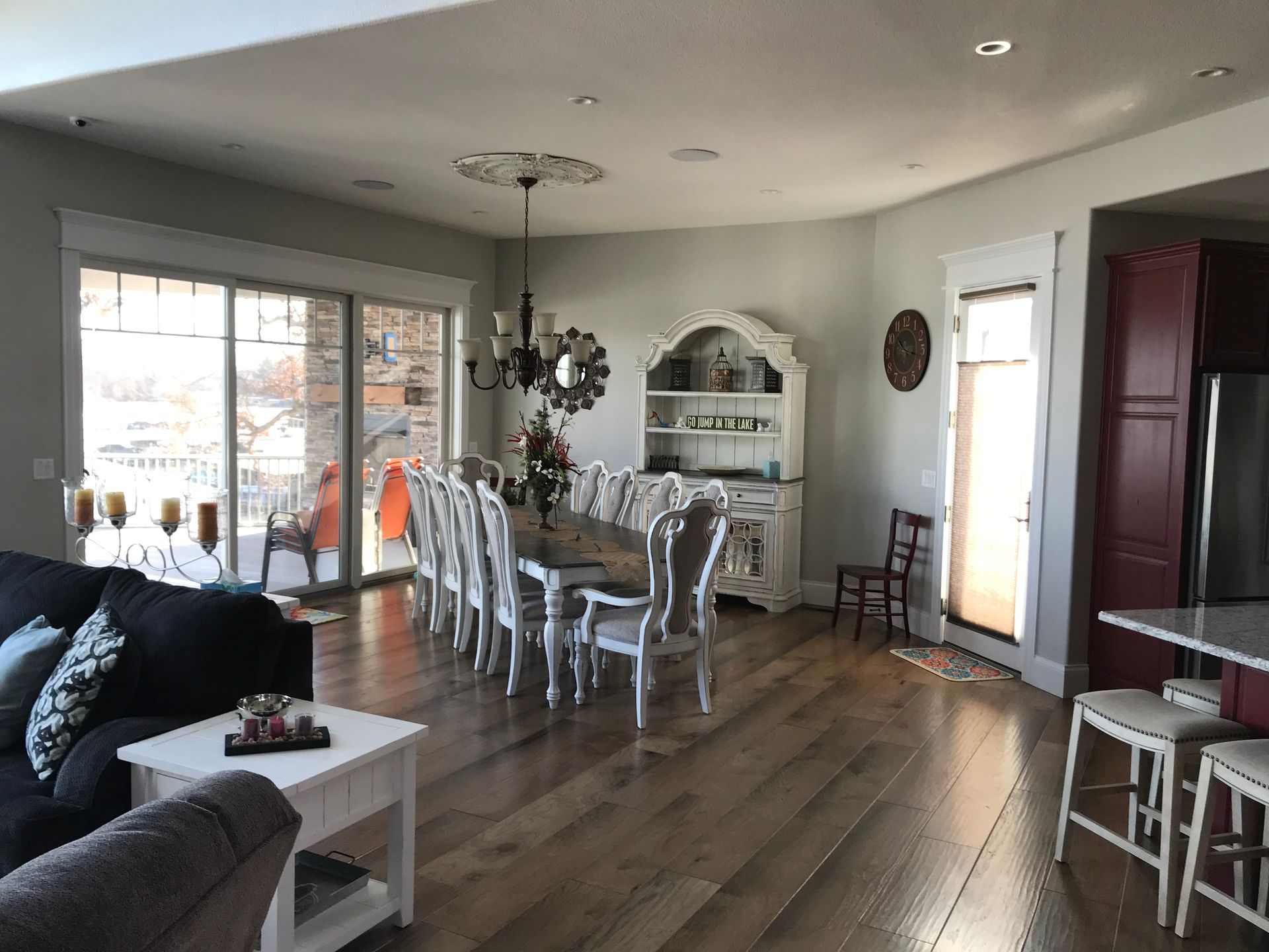 Open-plan dining room with long table, white chairs, hutch, and large windows.