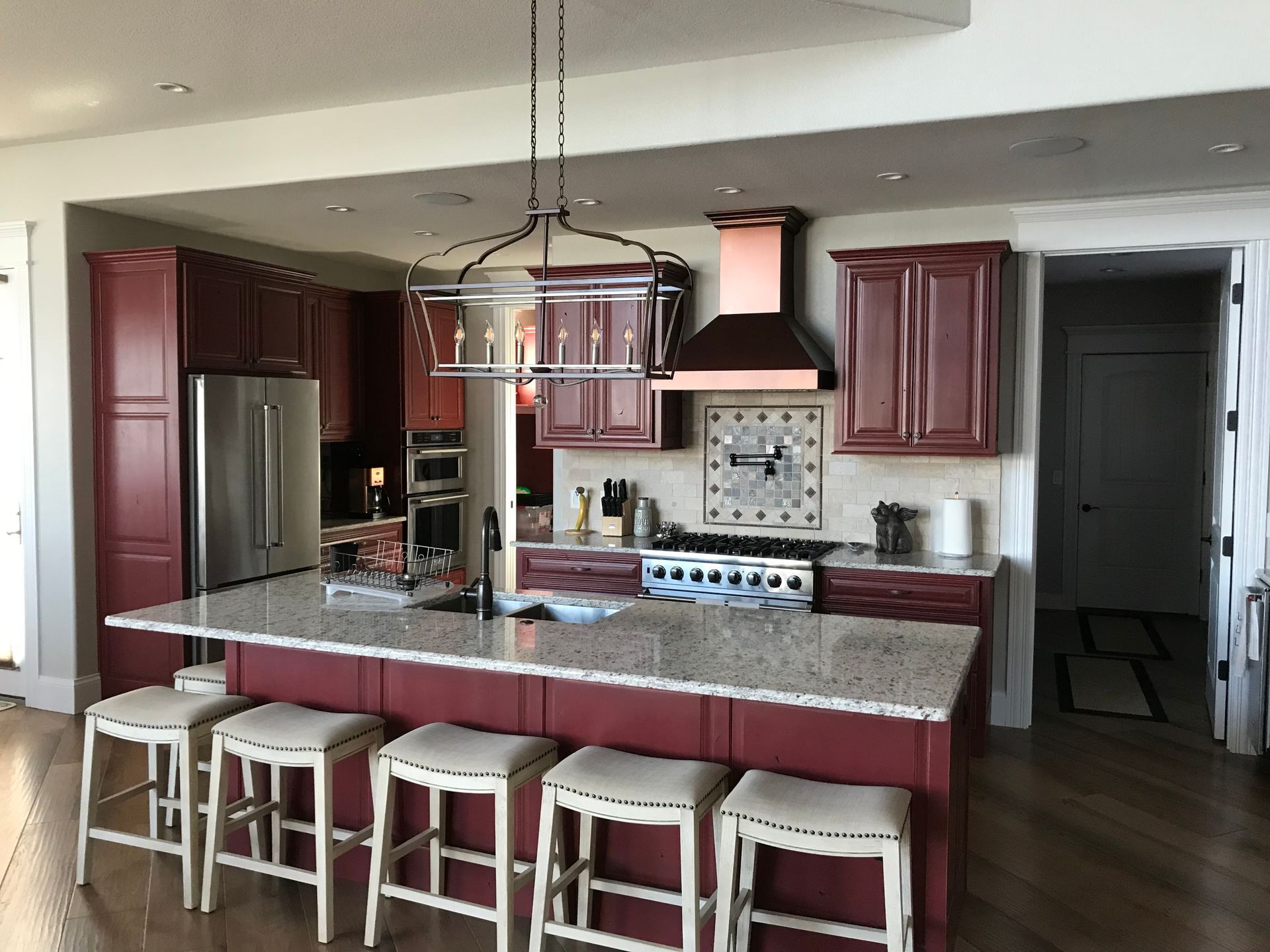 Modern kitchen with dark red cabinets, large island, bar stools, and hanging light fixture
