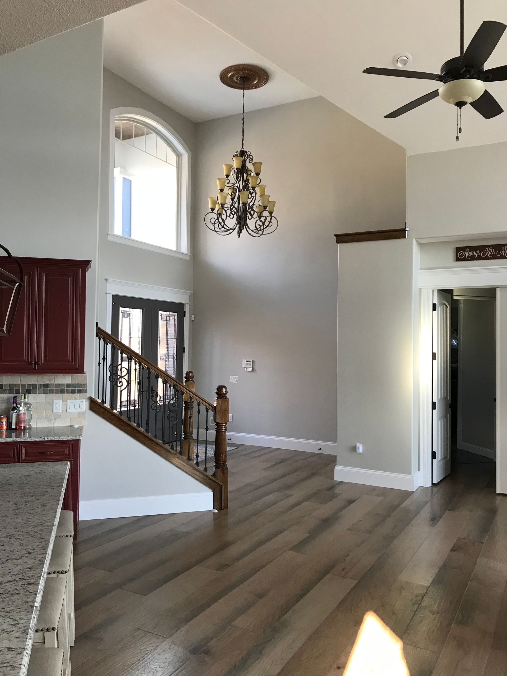 Open-concept living room with vaulted ceiling, chandelier, staircase, and ceiling fan near kitchen.