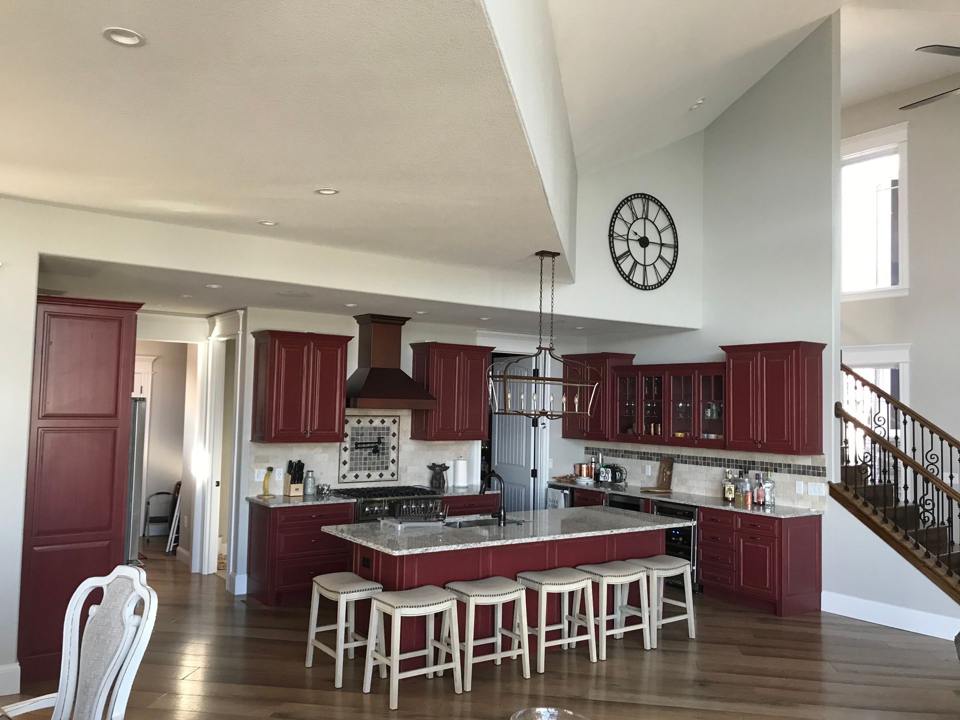 Modern kitchen with burgundy cabinets, central island, bar stools, and a staircase in the background