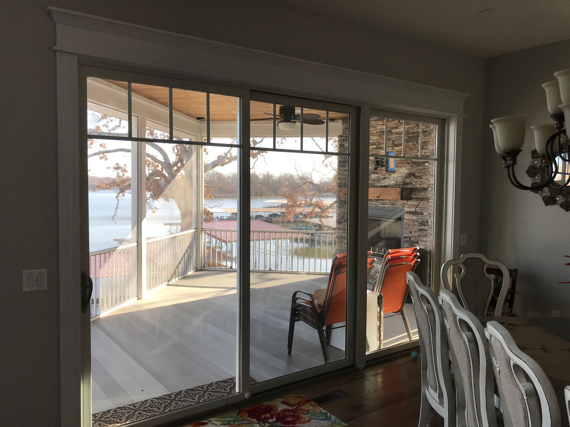 Dining room with sliding glass doors opening to a deck and lake view, with patio chairs and chandelier in foreground