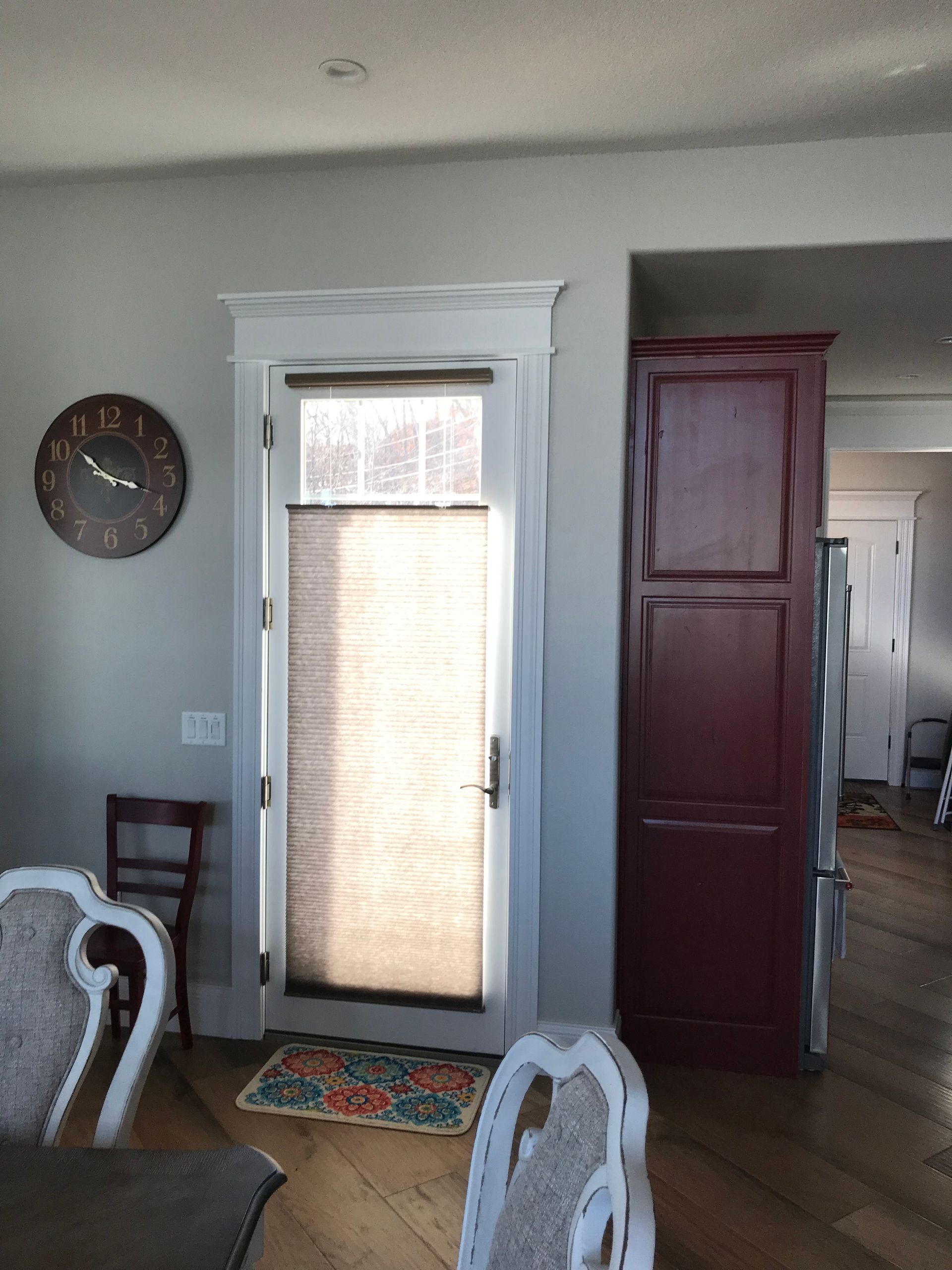 Living room with a glass door, wall clock, and tall maroon cabinet by a hallway