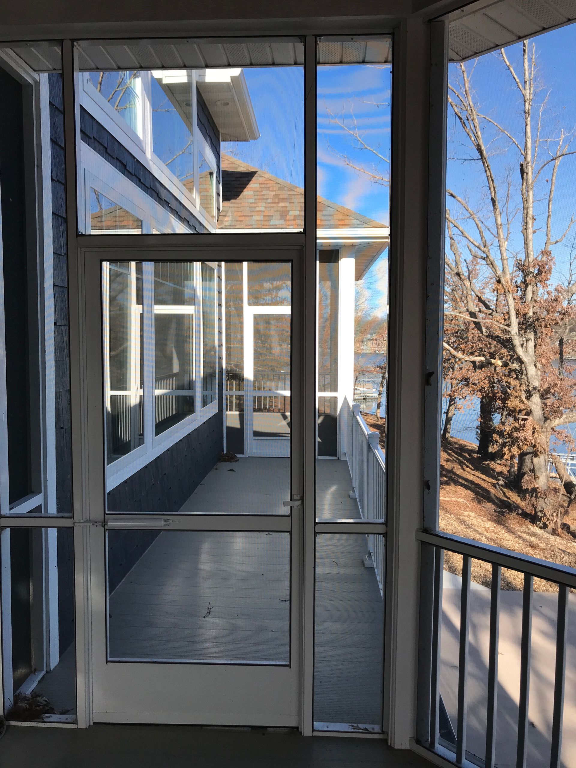 Covered apartment balcony with screened door, metal railing, and snowy trees outside