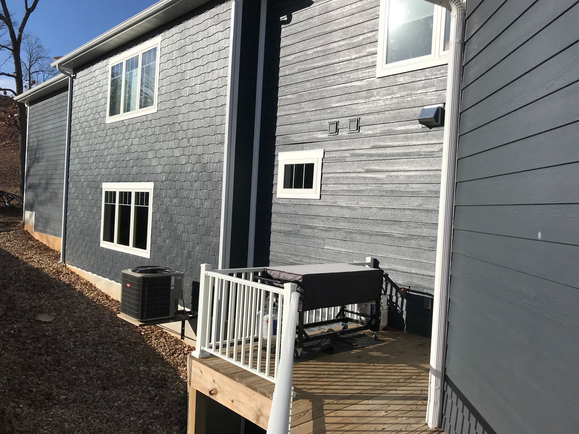 Gray townhouse exterior with a small wooden deck and white railing in a narrow side yard.