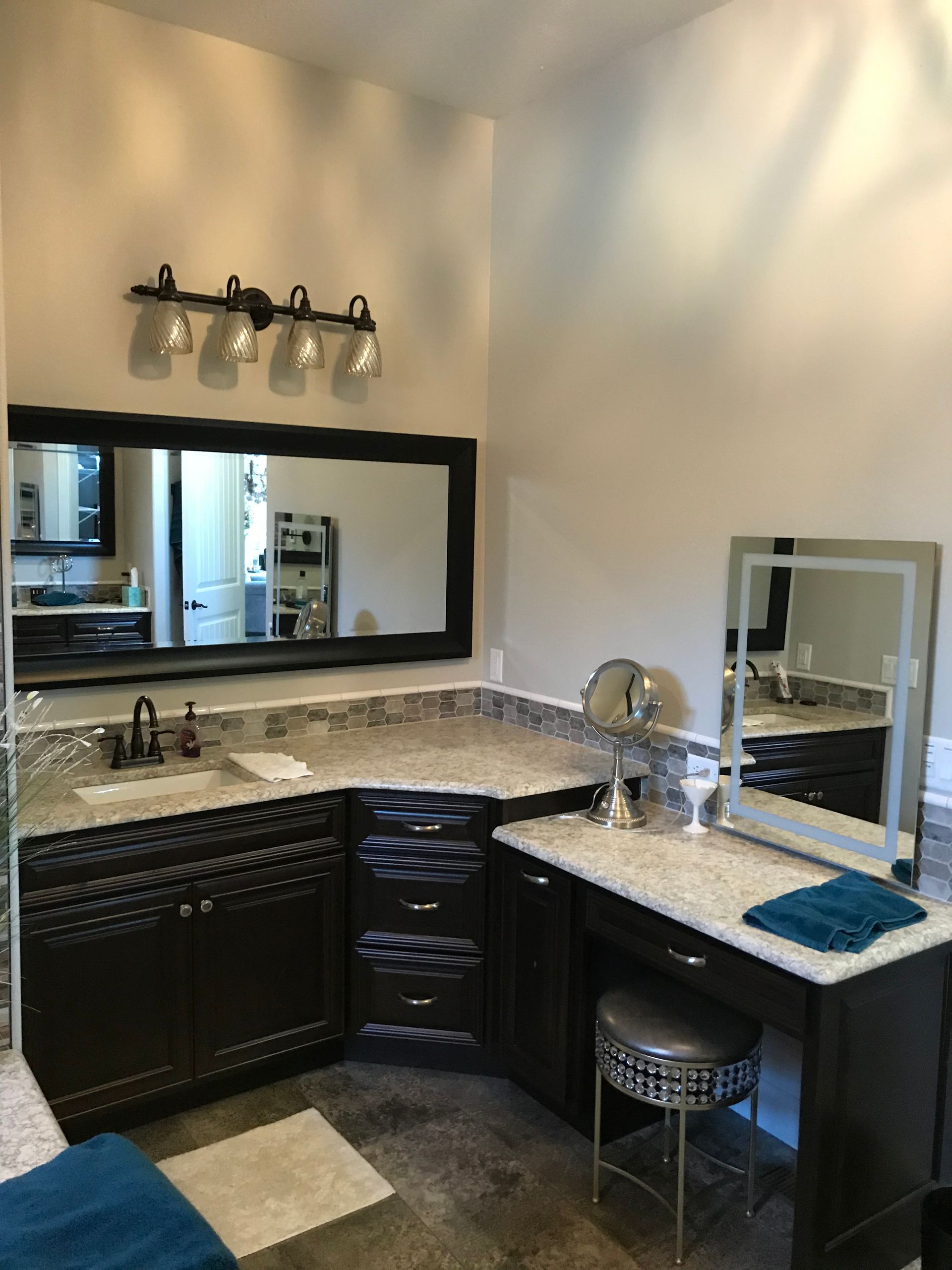 Modern bathroom vanity with dark cabinets, granite countertop, mirror, sink, and stool under wall lights