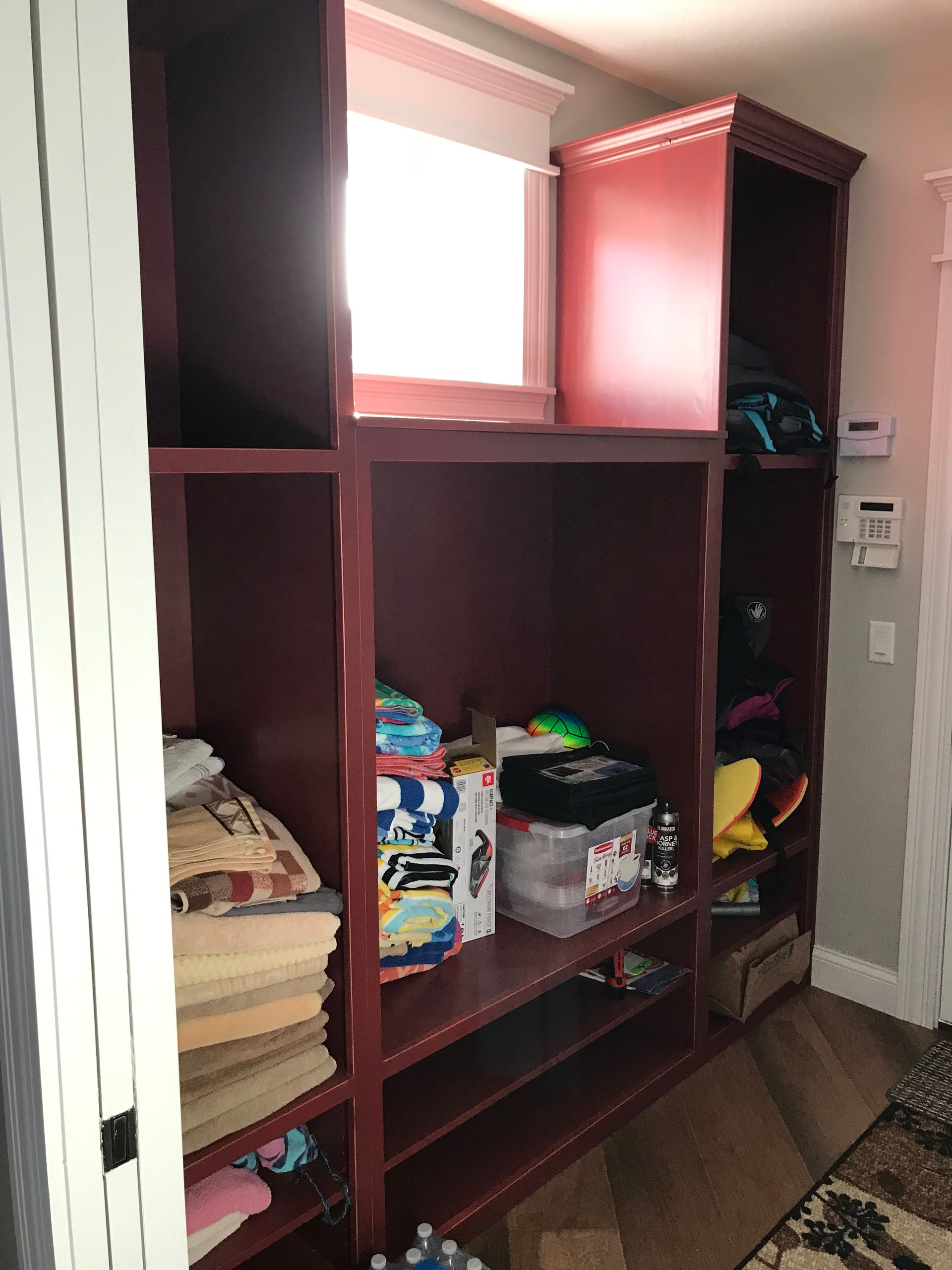 Wooden cubby shelving with folded clothes and bins in a small room by a window