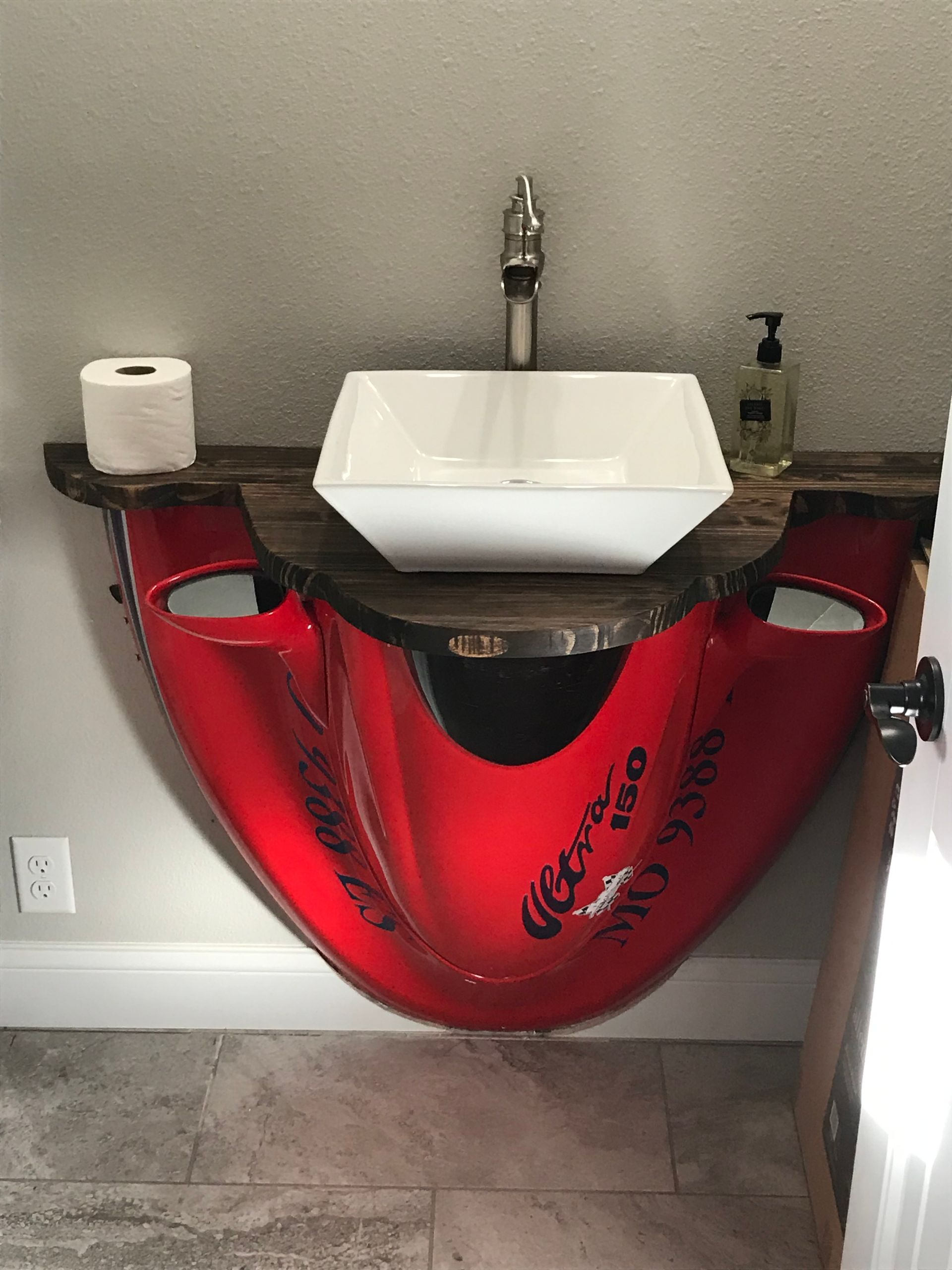 Small sink with red Coca-Cola can cabinet in a bathroom or bar area, with toilet paper on the left.