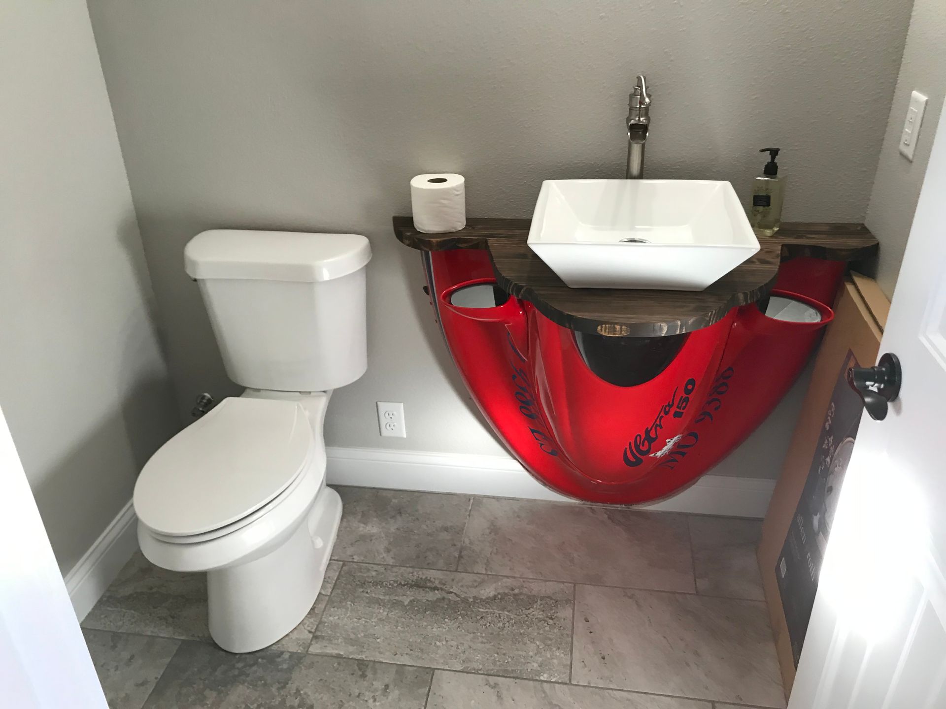 Small bathroom with toilet and vessel sink over a red vanity skirt on a gray tiled floor.