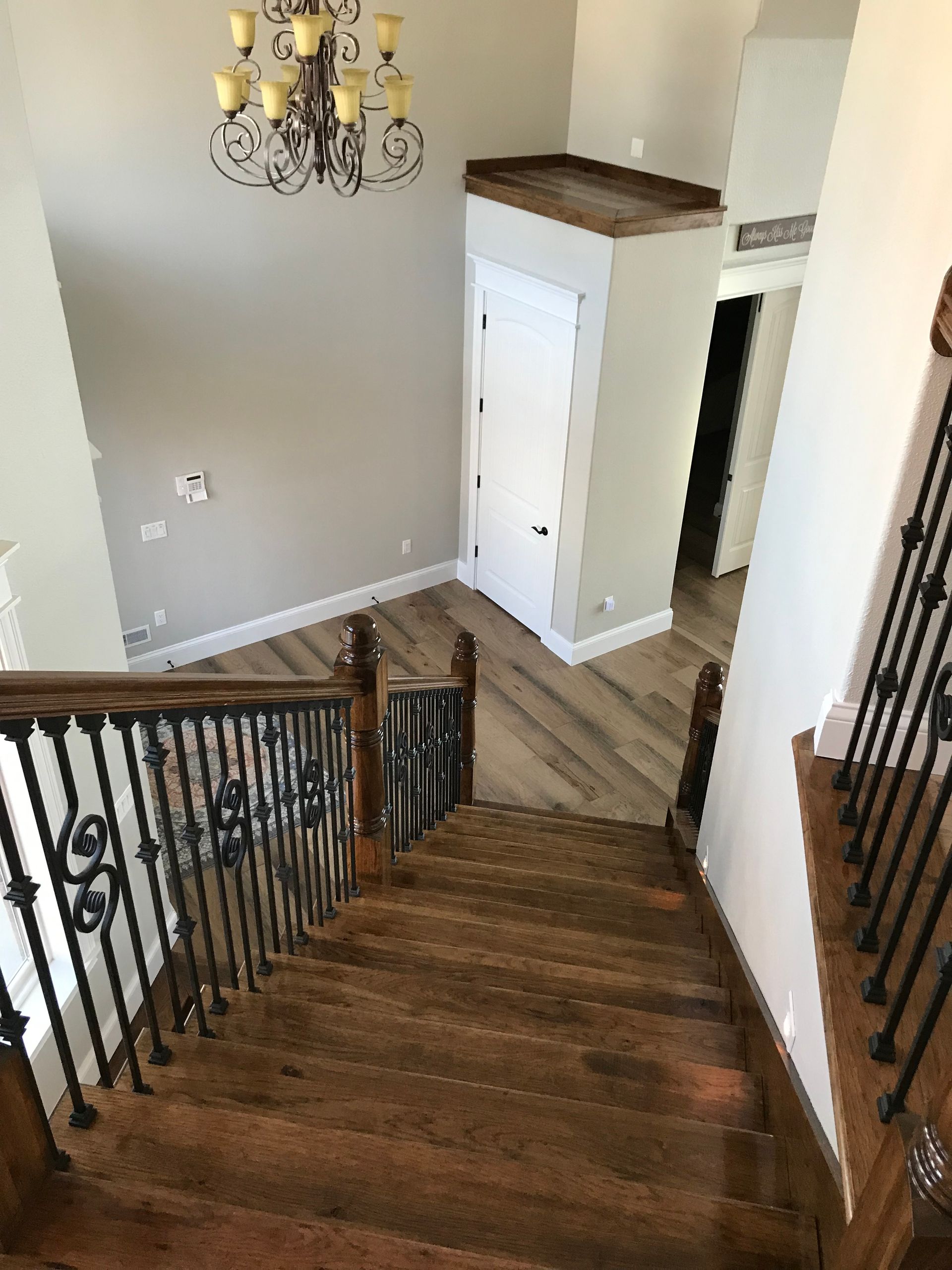 Staircase with wooden steps, black iron railings, and a chandelier in a bright entryway.