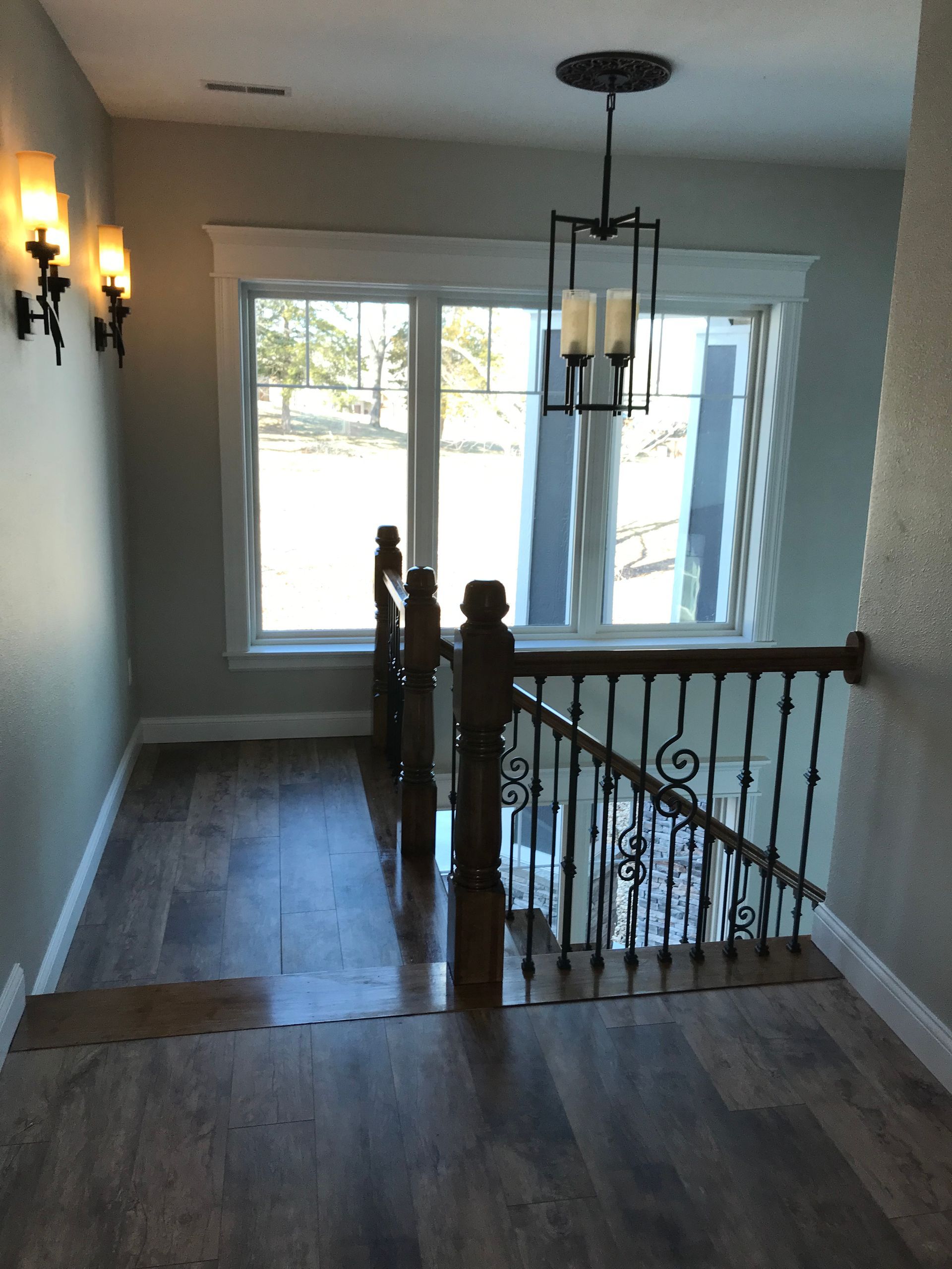 Upstairs hallway with wood floors, chandelier, staircase railing, and bright windows overlooking outside.