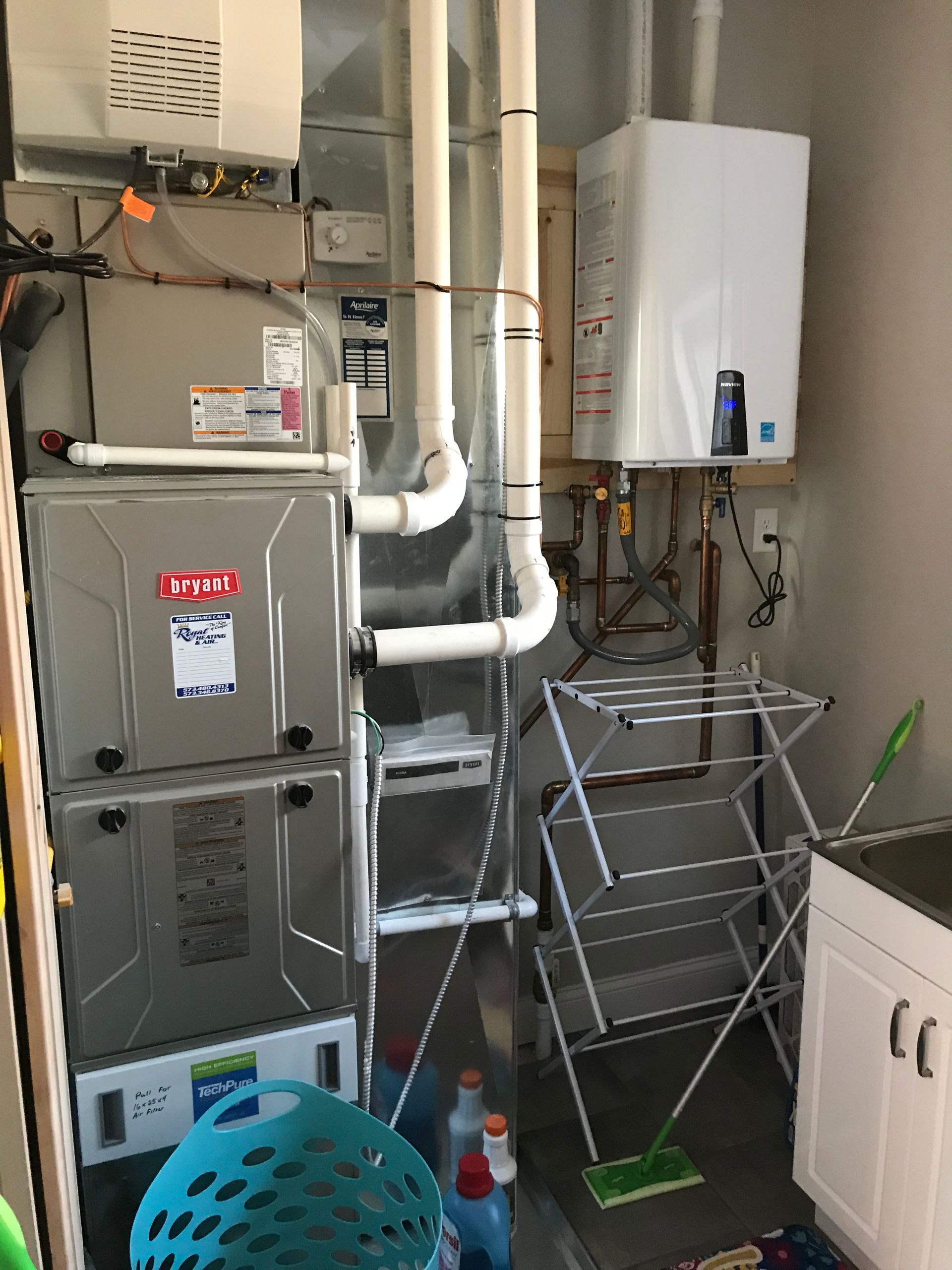 Basement utility room with furnace, water heater, white pipes, drying rack, and cleaning items