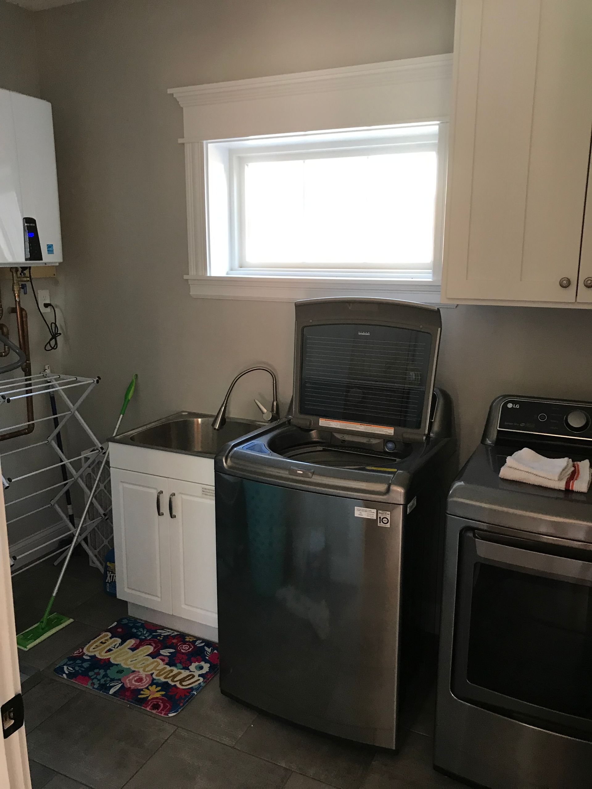 Small kitchen with stainless steel sink, dishwasher, oven, white cabinets, and a window above the counter.