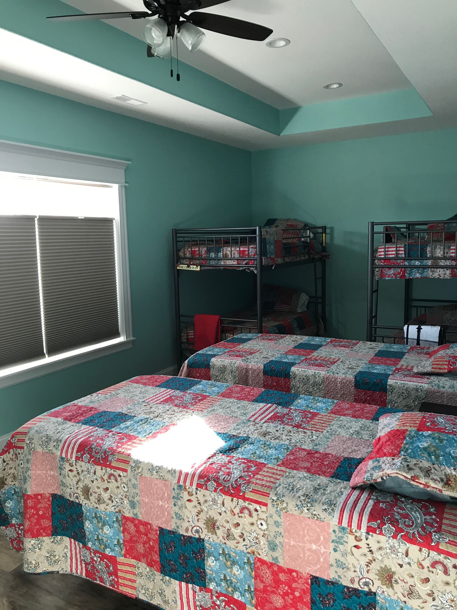 Bedroom with teal walls, a patchwork bedspread, ceiling fan, and window blinds.