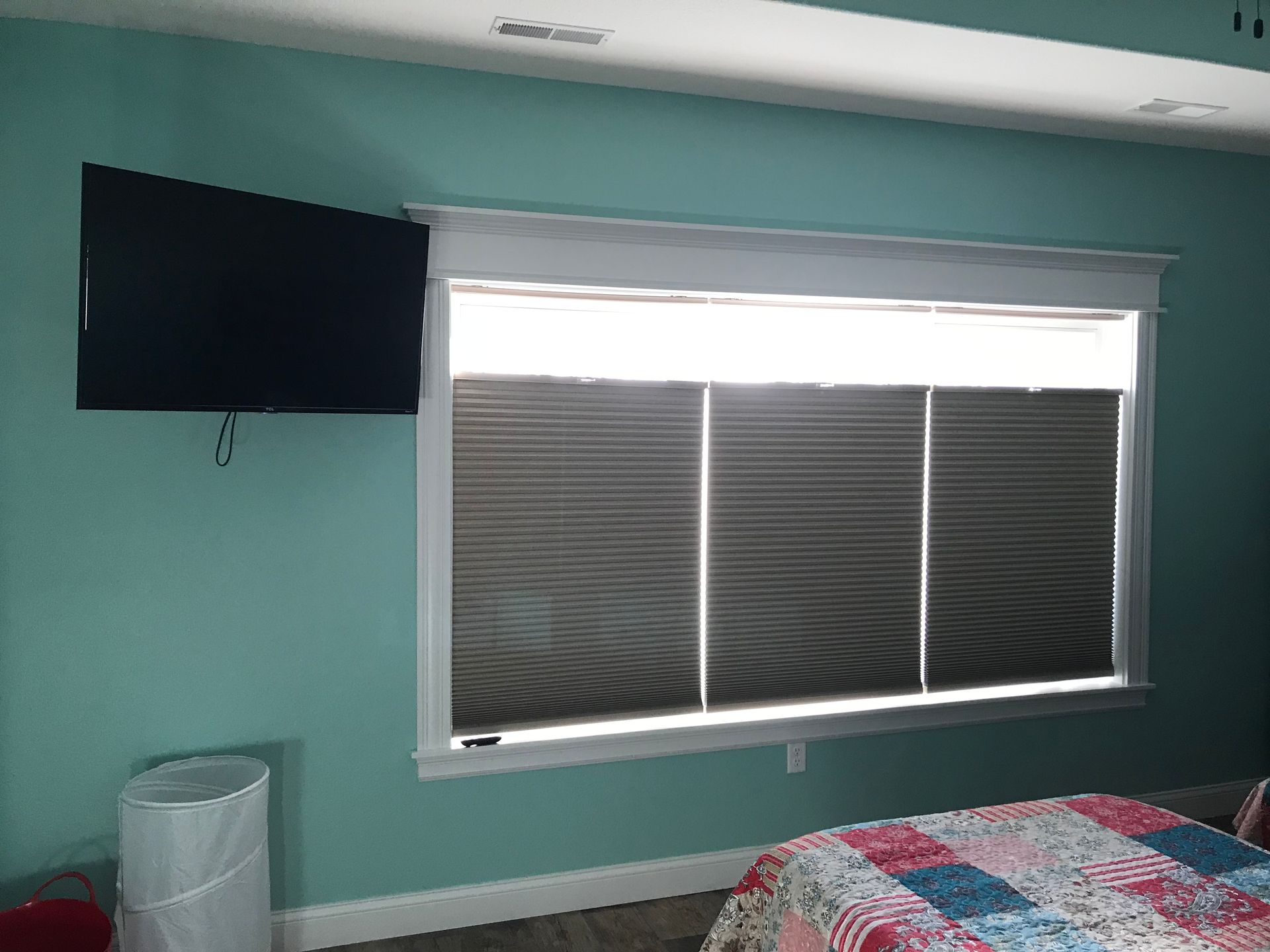 Bedroom with teal walls, wall-mounted TV, window with blinds, and a bed with a red patterned blanket.