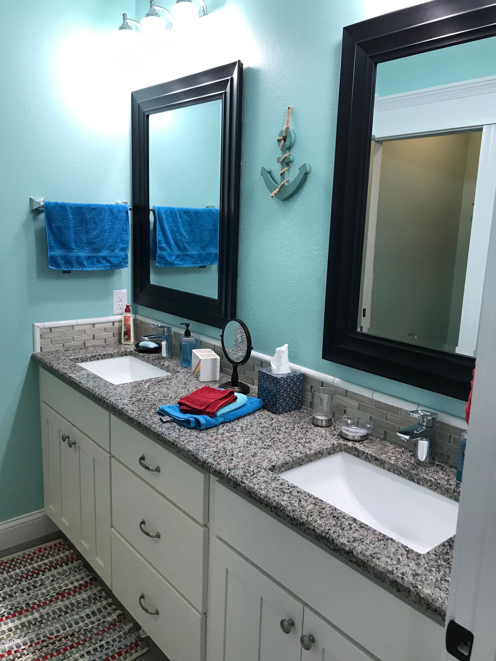 Bathroom vanity with double sinks, granite countertop, large black mirror, and blue towels on a pale wall