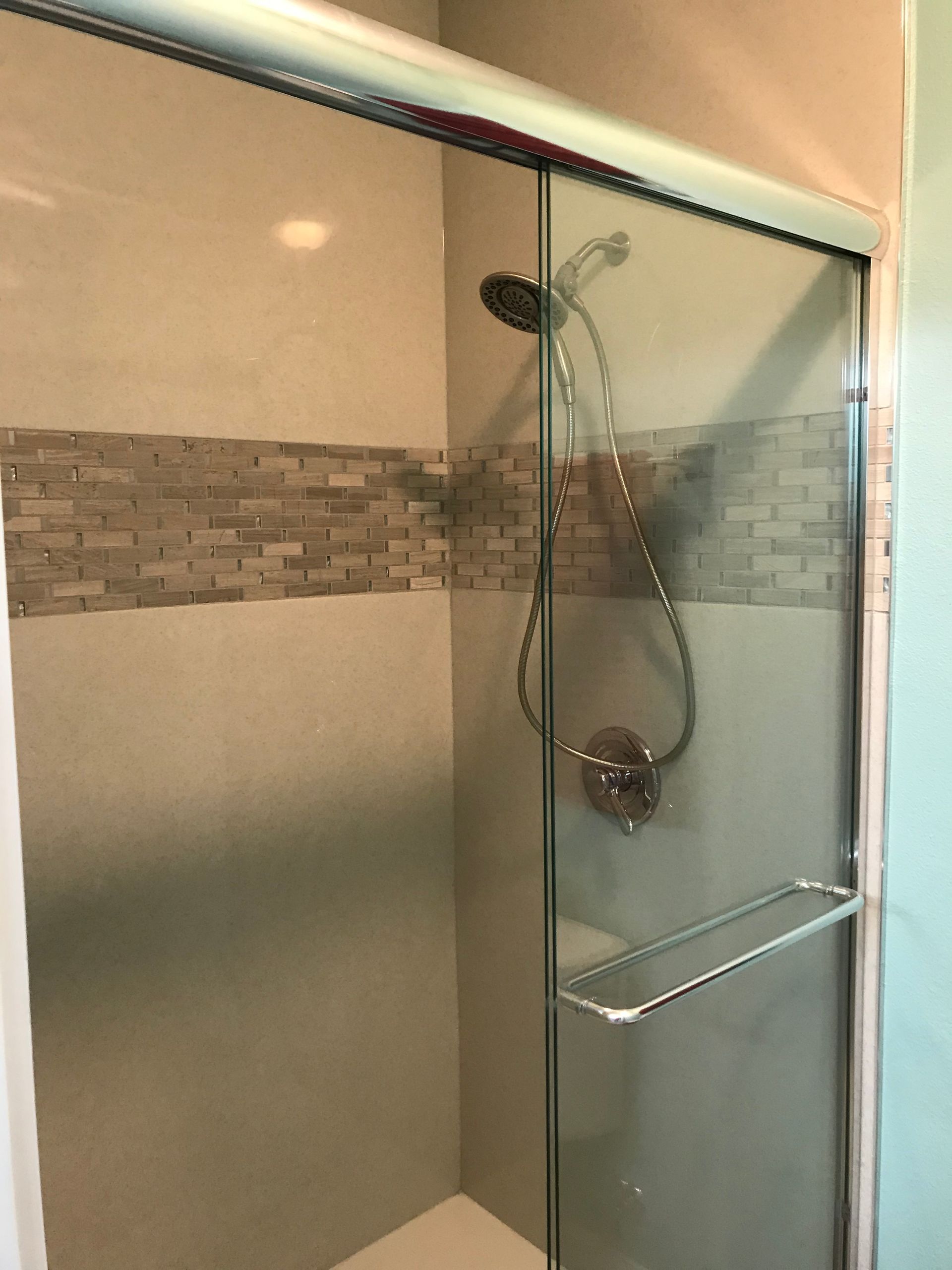 Glass shower stall with chrome fixtures and mosaic tile accent strip in a bathroom