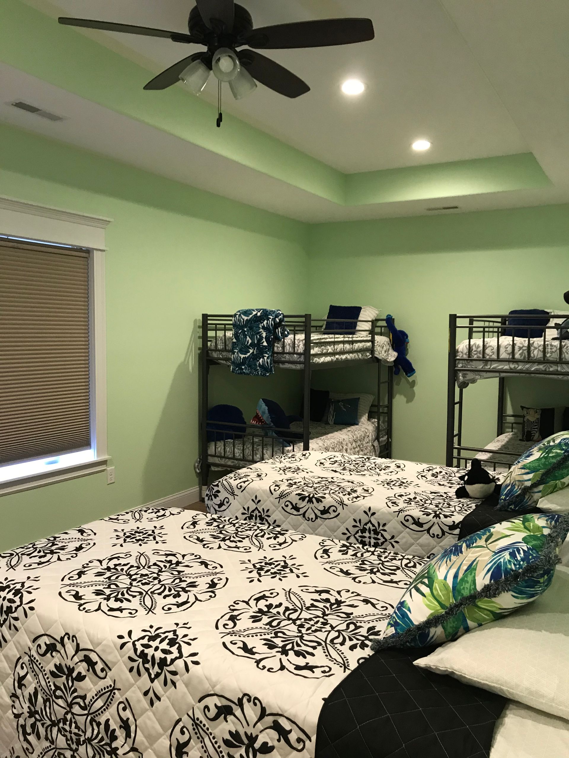Mint-green bedroom with a bed, ceiling fan, shelves, and a window with blinds.