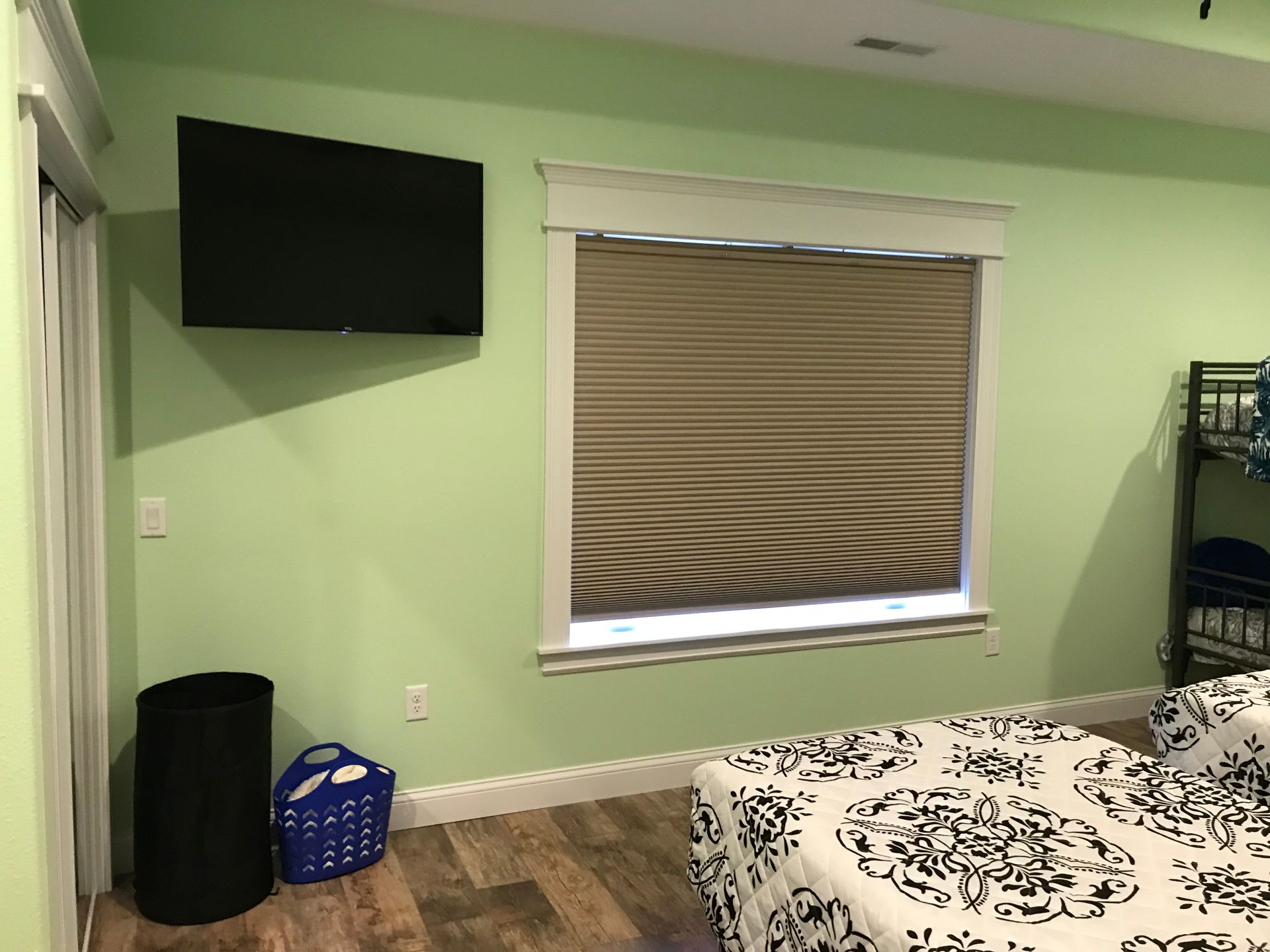 Bedroom with green walls, wall-mounted TV, window shade, and patterned bedspread.