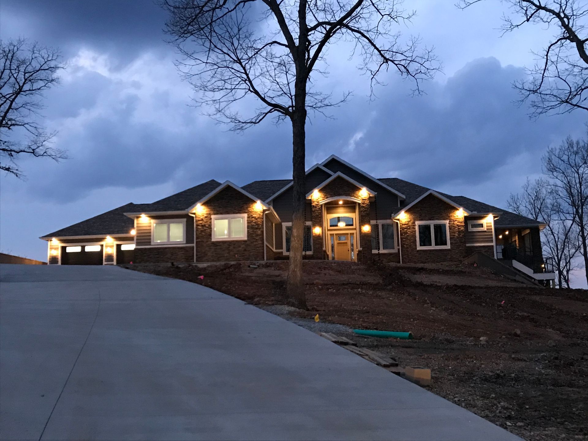 Brick house with warm porch lights at dusk, set on a sloped driveway under a cloudy sky