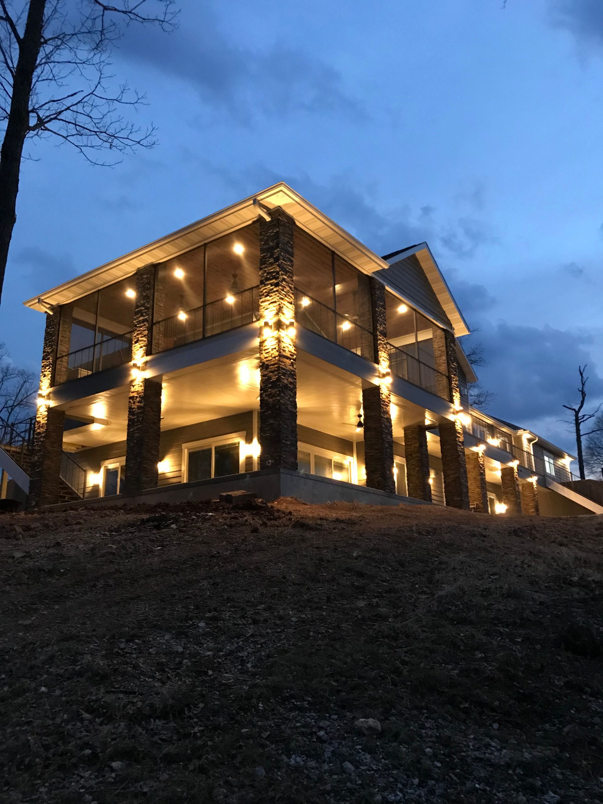 Two-story house at dusk, warmly lit with string lights on a hillside