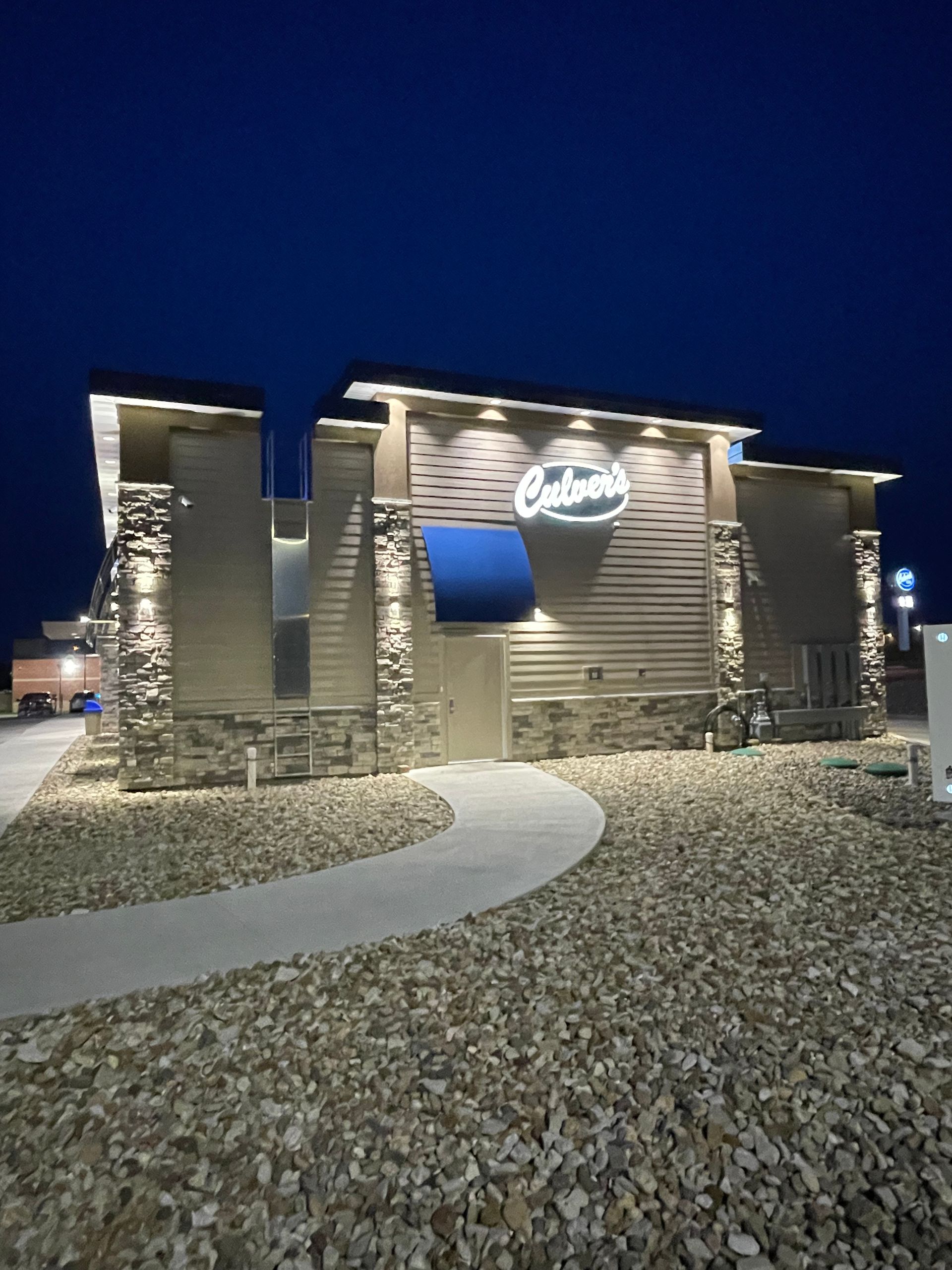 Illuminated stone entrance sign at night with a curved walkway under a dark blue sky