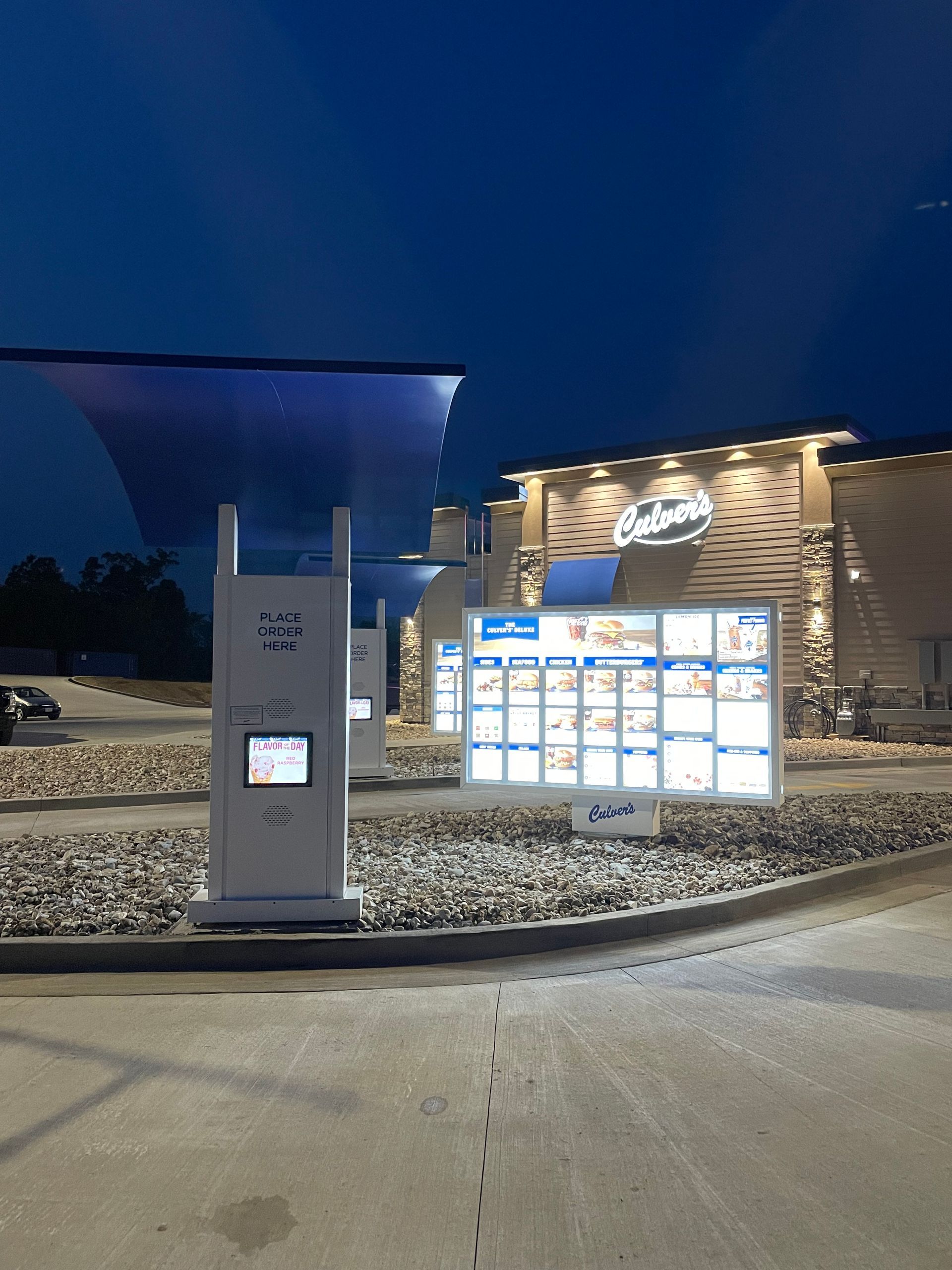 Nighttime outdoor drive-through menu board and ordering kiosk lit up outside a restaurant.