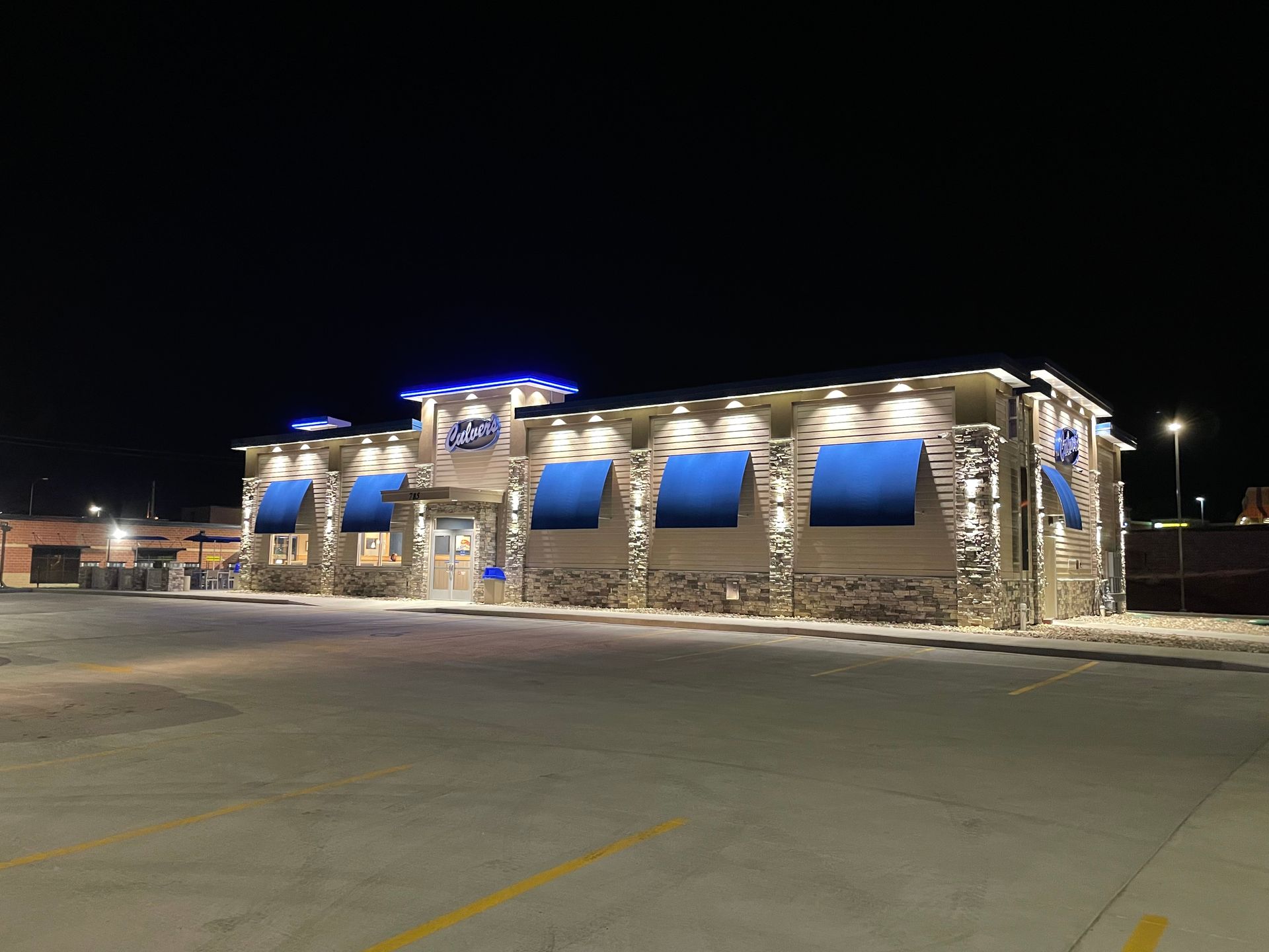 Stone-faced restaurant at night with blue awnings and bright exterior lights in an empty parking lot