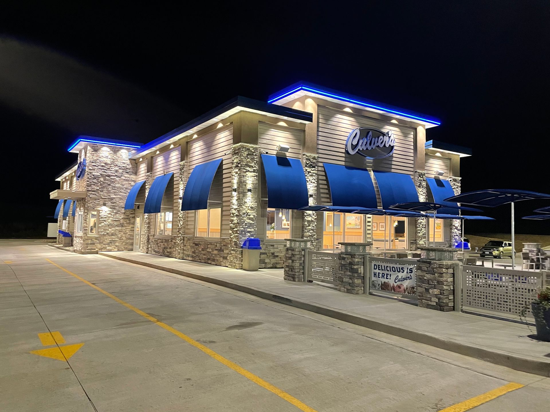 Stone restaurant building at night with blue awnings and neon roof trim, lit in an empty parking lot