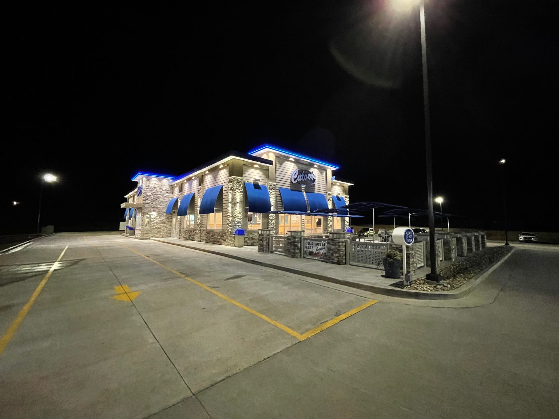 Nighttime view of a blue-lit building with an empty parking lot and streetlights.