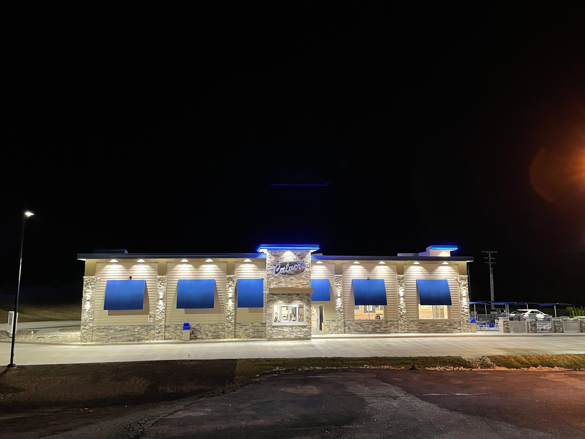 Nighttime exterior of a small stone building with blue-lit windows and a lit entrance under the dark sky