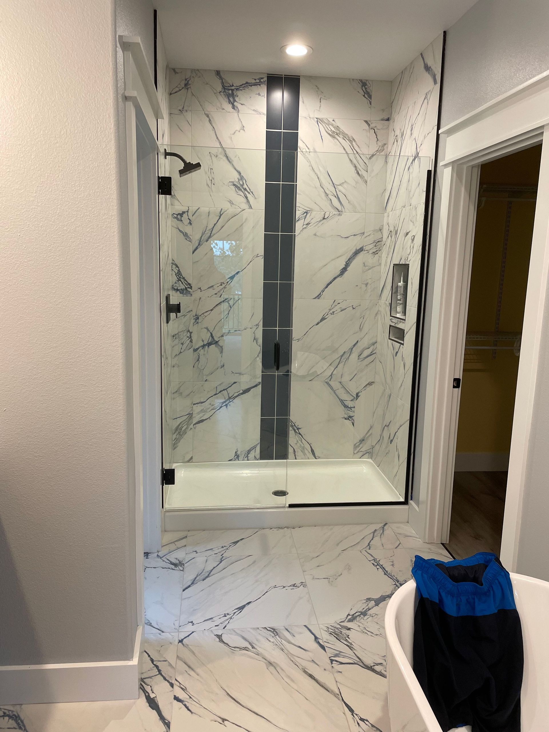 Modern bathroom with marble shower, glass door, and a white bathtub in the foreground