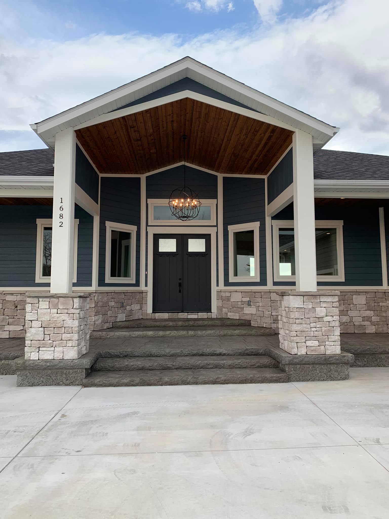 Front entrance of a building with stone steps, dark doors, white columns, and blue siding