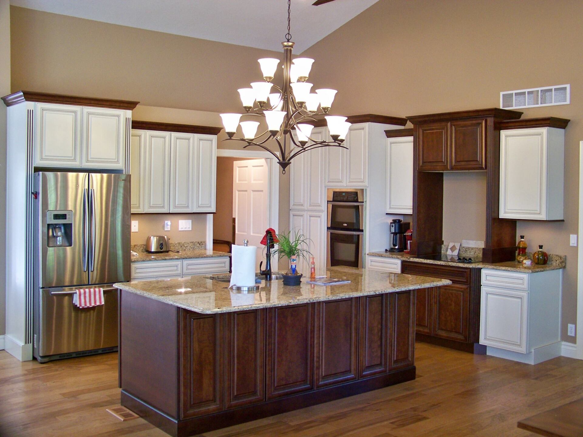 Spacious modern kitchen with dark wood cabinets, granite island, stainless fridge, and chandelier lighting