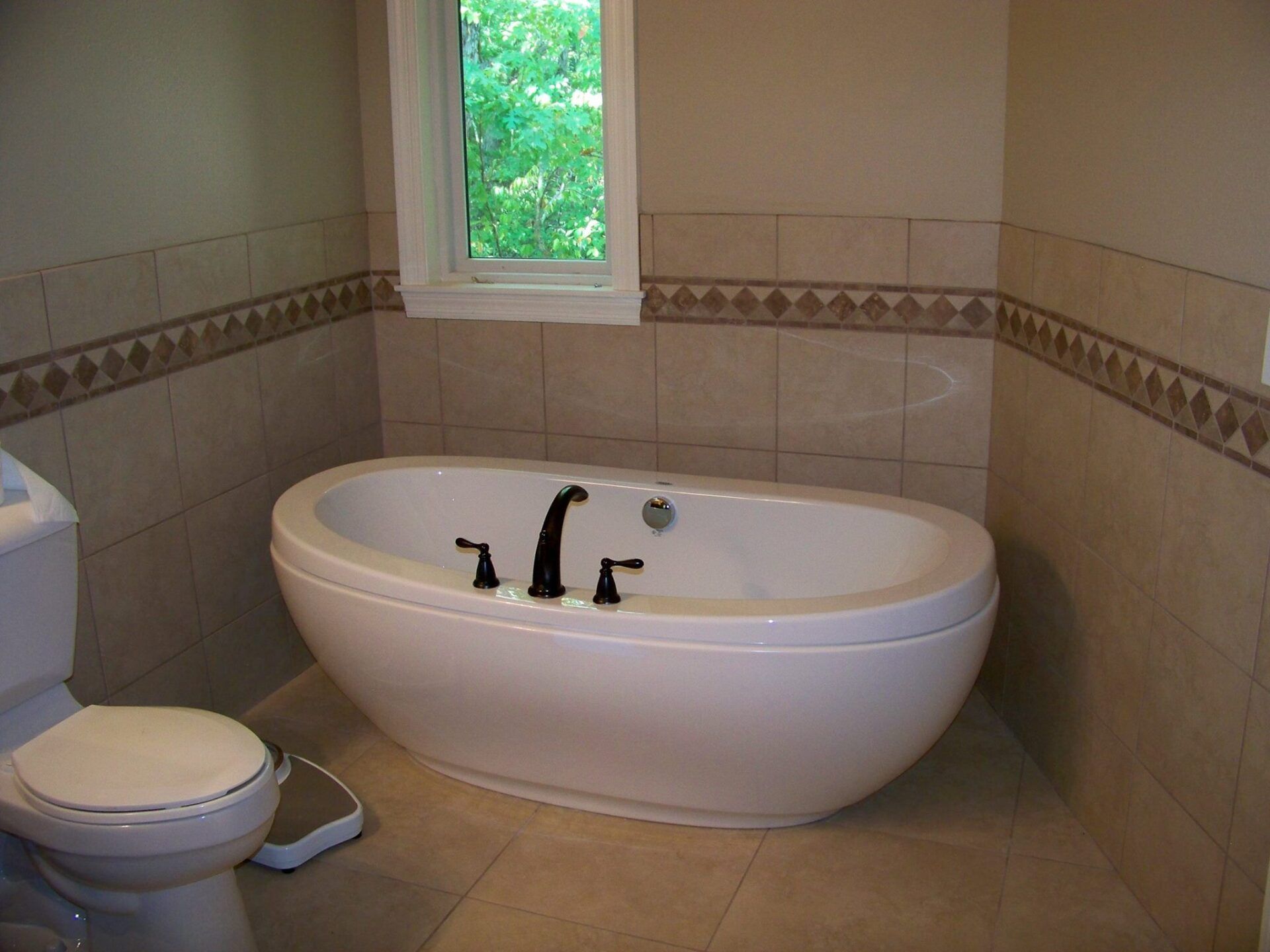 Bathroom with a toilet, large oval soaking tub, tiled walls, and a small window above the tub