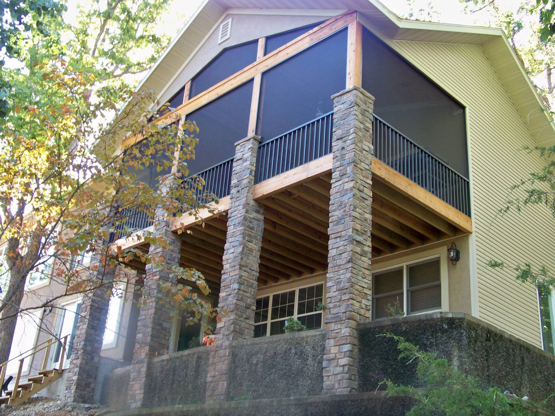 Wooden cabin with stone pillars and a covered balcony under trees
