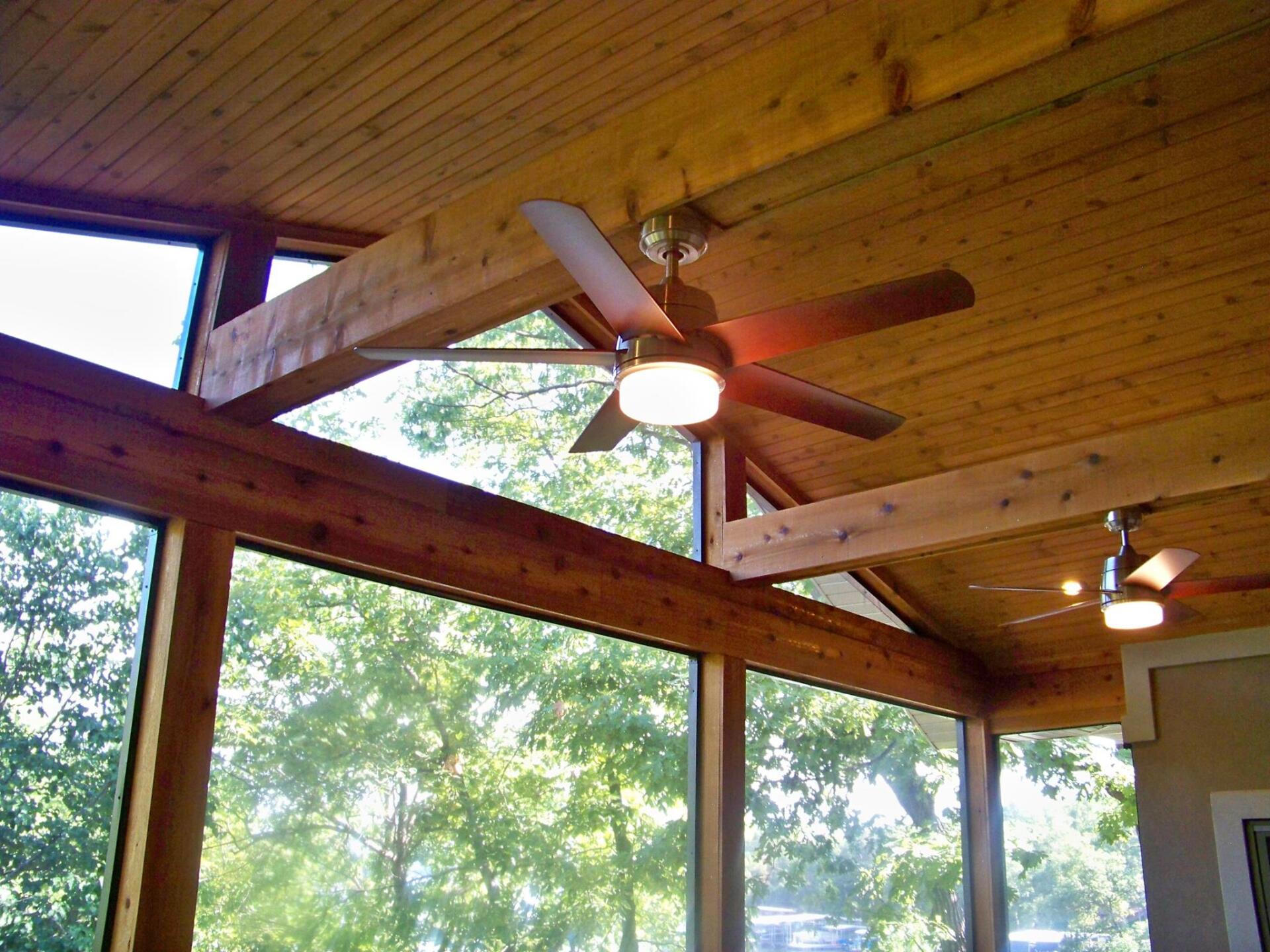 Wood-paneled screened porch with vaulted ceiling, ceiling fans, and large windows overlooking trees