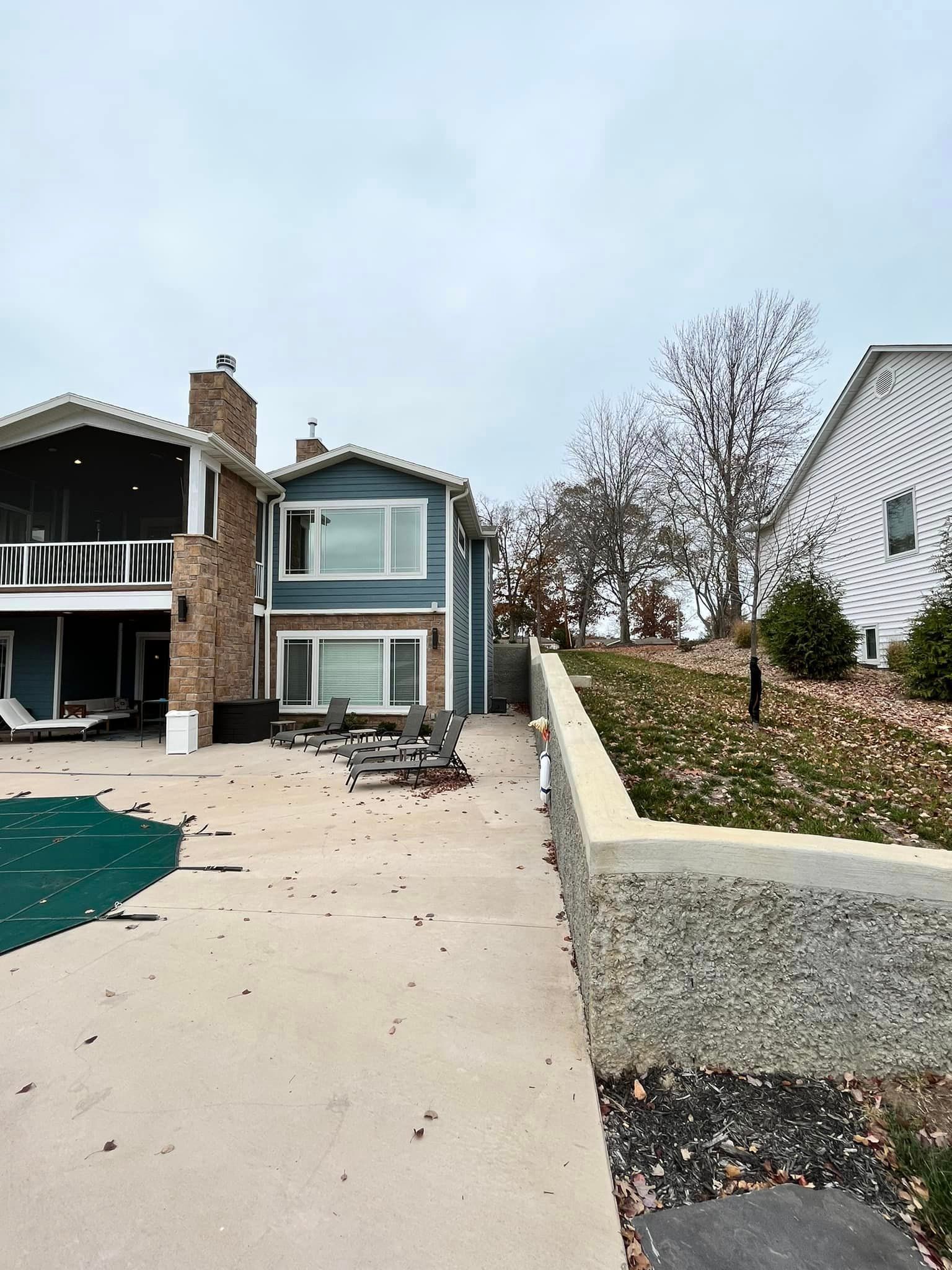 House with concrete driveway beside a sloped retaining wall and leafless trees