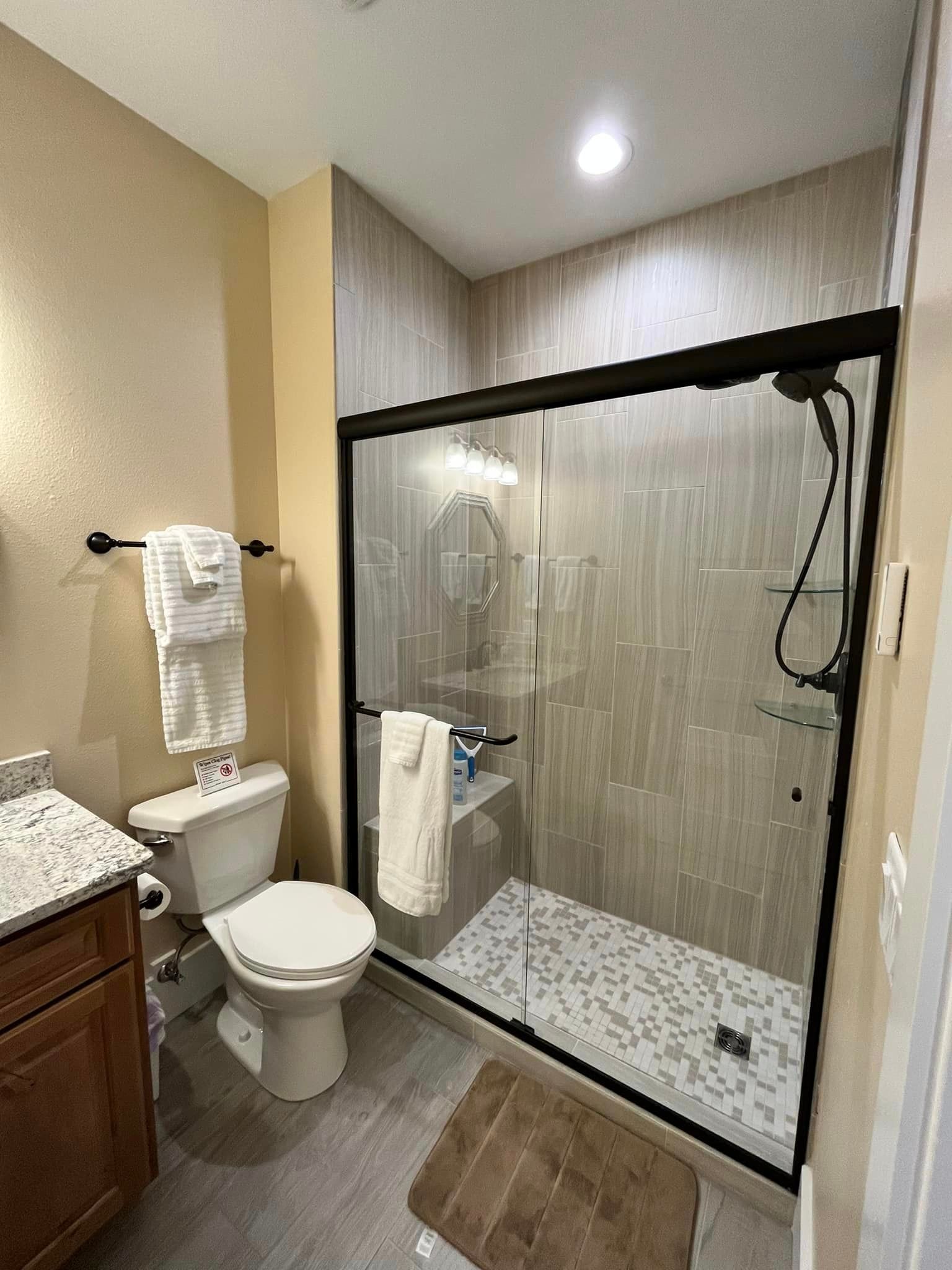 Small bathroom with a glass shower, toilet, sink vanity, and tan tile walls.
