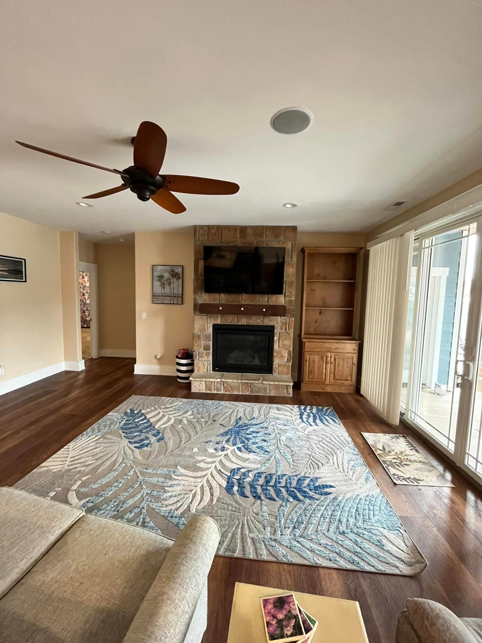 Living room with fireplace, wall-mounted TV, ceiling fan, patterned rug, and sliding glass doors