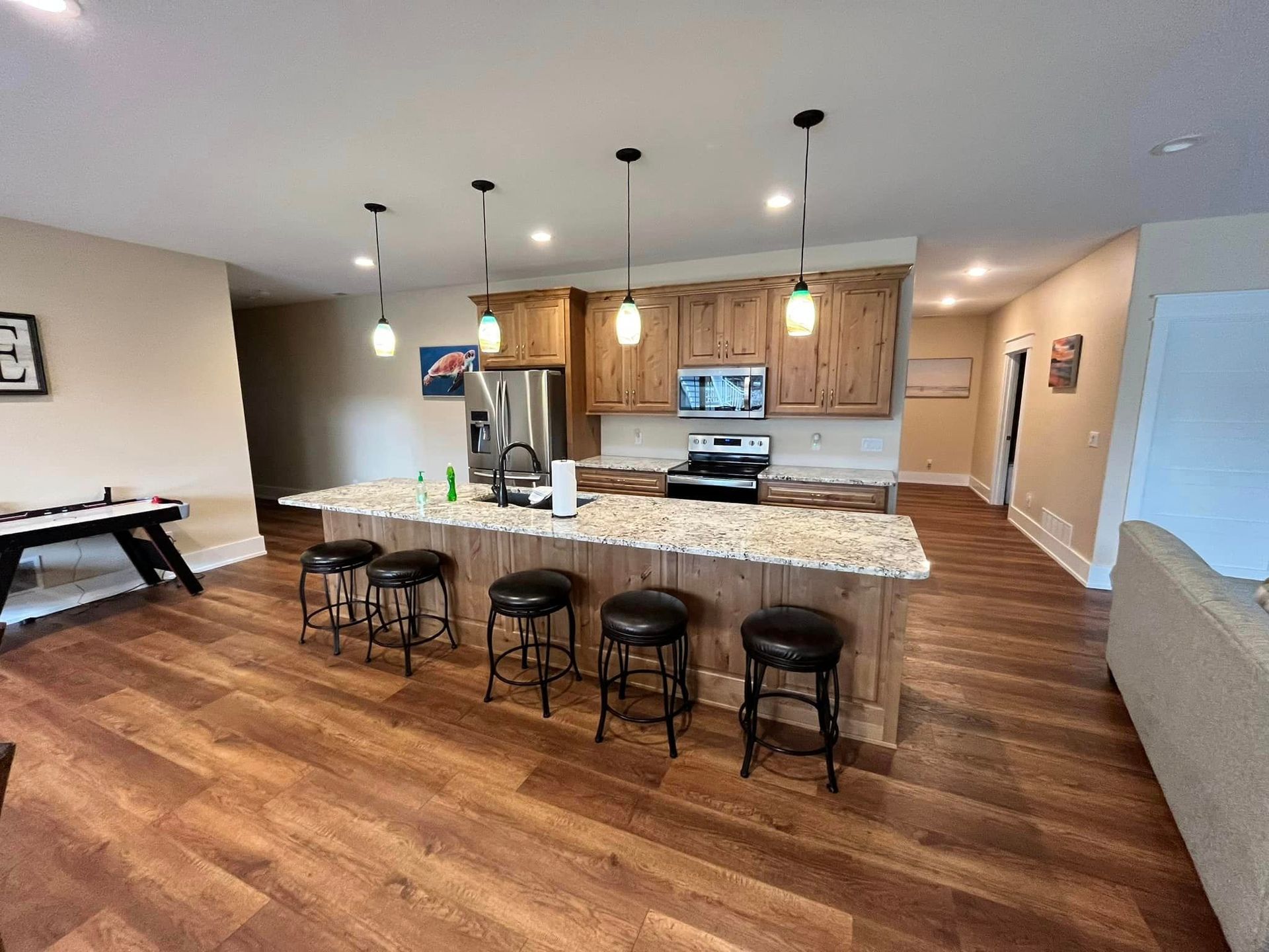Open kitchen and living area with granite island, bar stools, wood cabinets, and hardwood floors