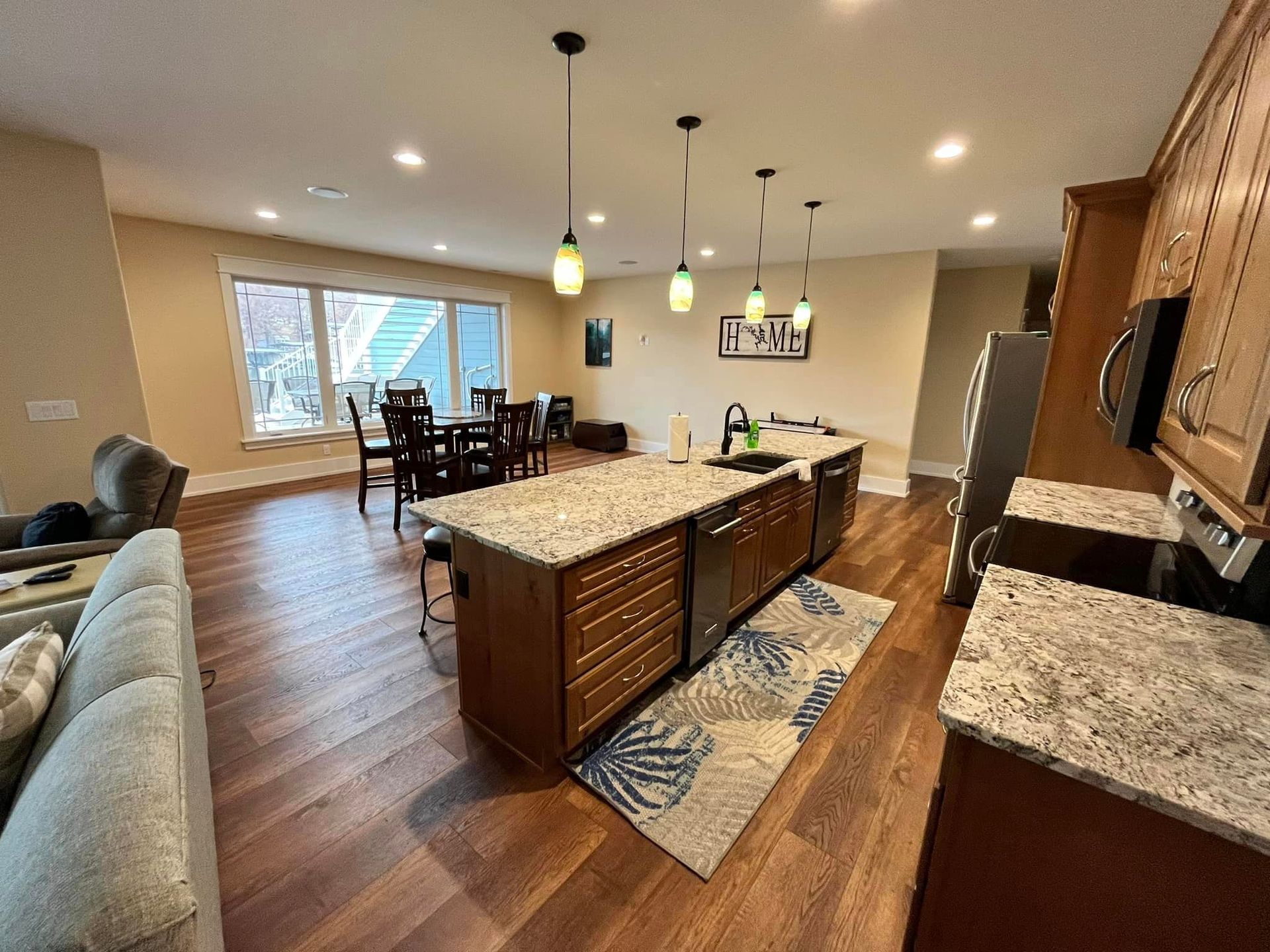 Open-concept kitchen and dining room with granite island, wood floors, and large windows